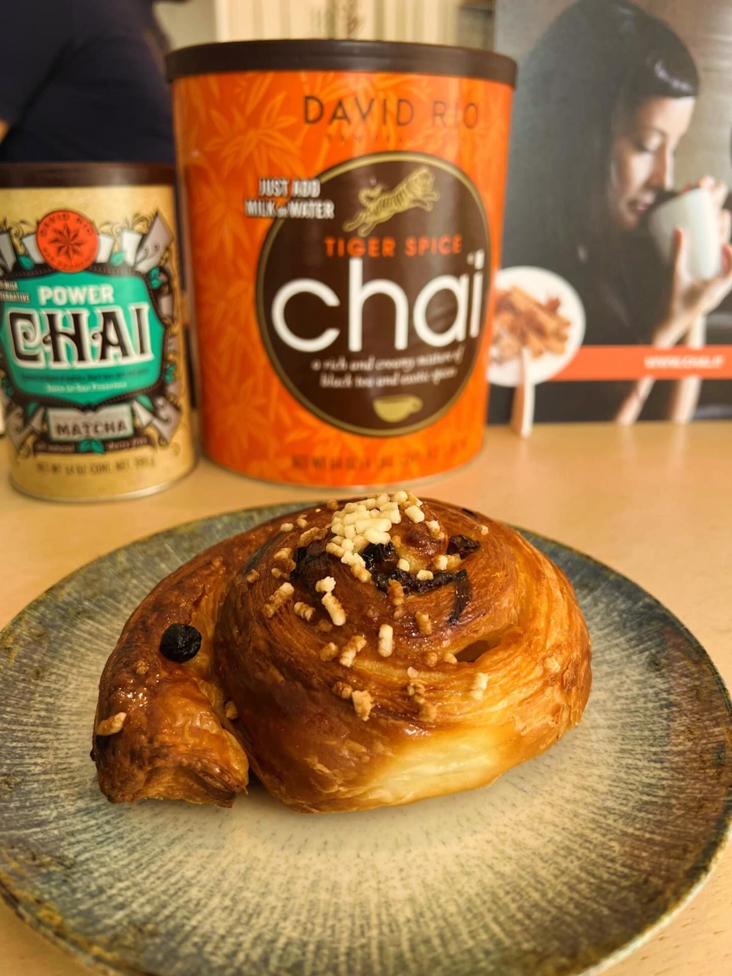 Una sfoglia dorata ricoperta di noci è adagiata su un piatto dalla superficie ruvida, con due contenitori di polvere di chai sullo sfondo.