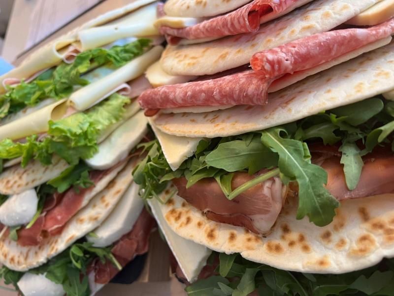Primo piano di panini piatti italiani impilati e farciti con salumi, mozzarella fresca e rucola.