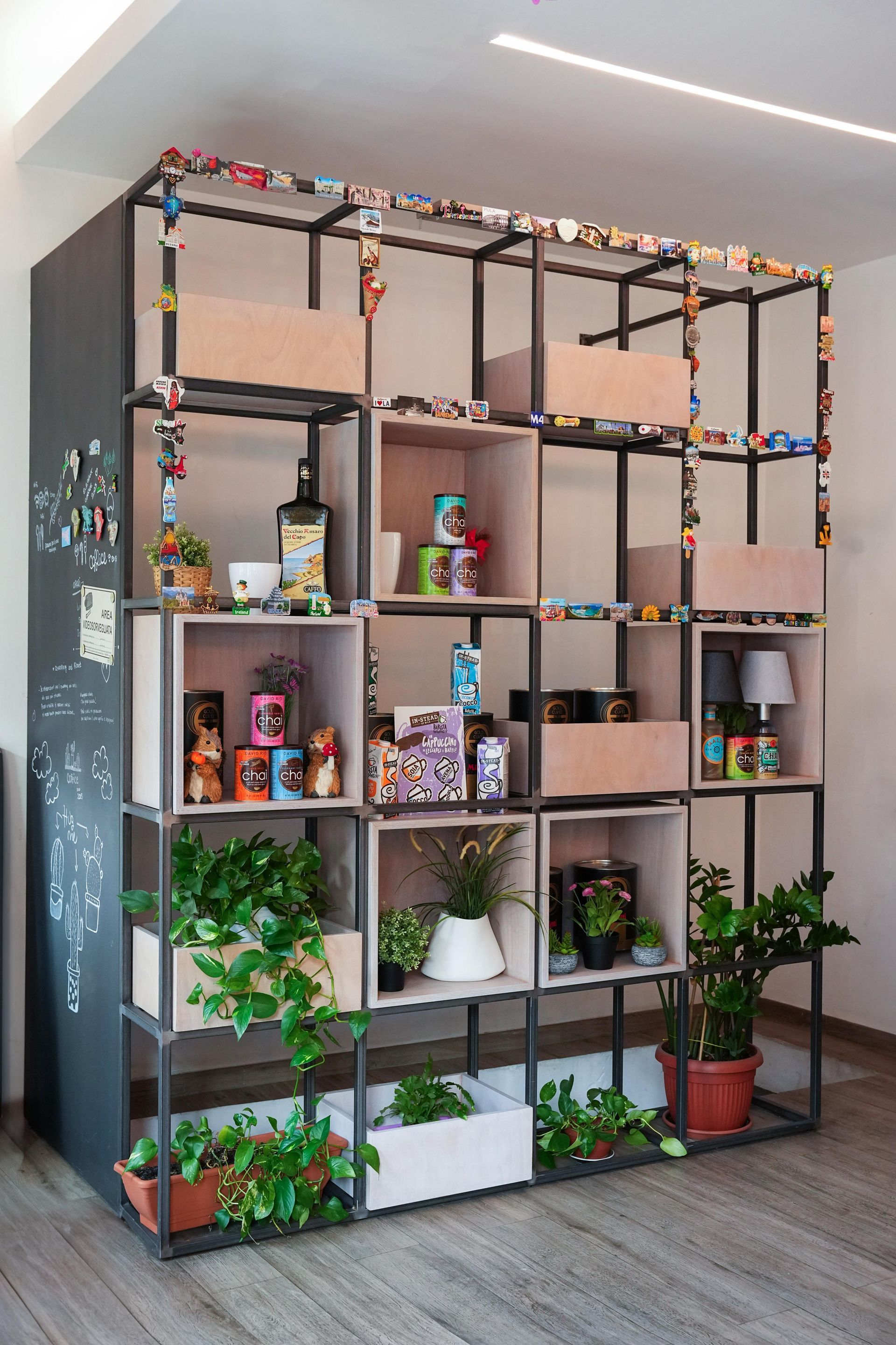 Scaffalatura metallica aperta con contenitori in legno per piante, oggetti decorativi e pannello laterale con lavagna.