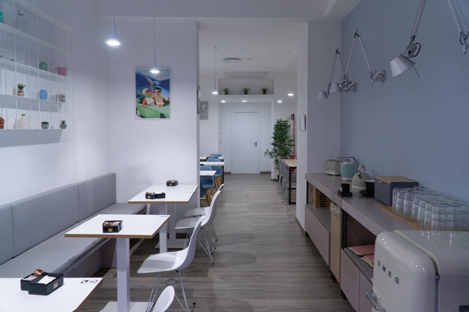 L'interno di una caffetteria moderna e minimalista presenta pareti bianche, panche imbottite grigie, tavolini e un elettrodomestico color crema.