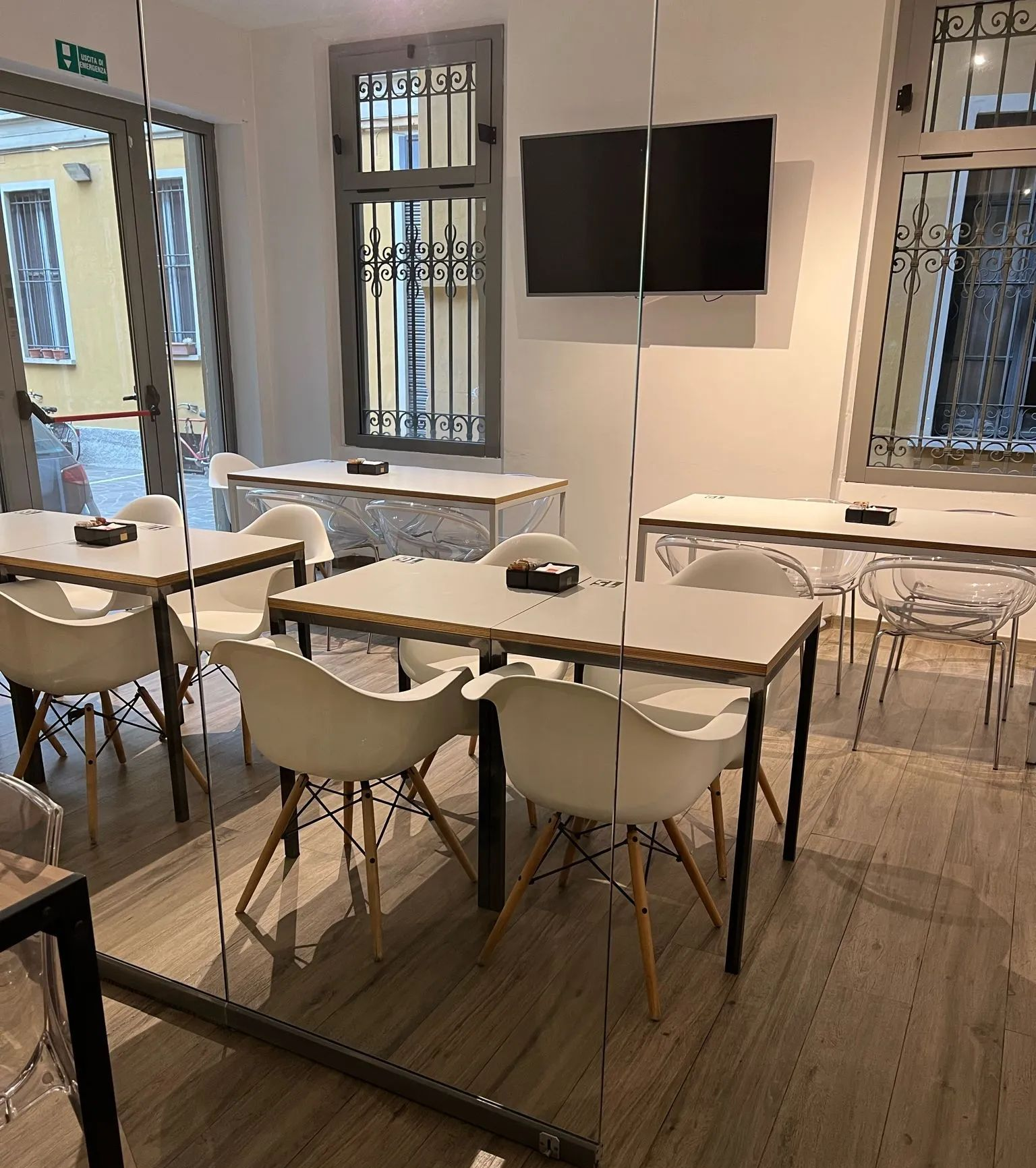 Area interna moderna del bar con tavoli, sedie bianche sagomate e televisore a schermo piatto montato a parete.