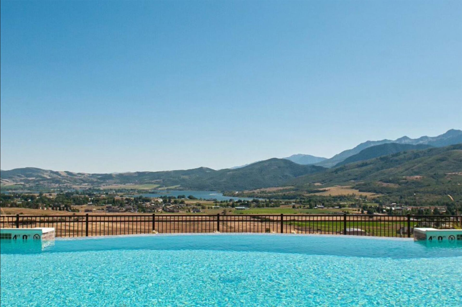 A large swimming pool with a view of mountains and a lake.