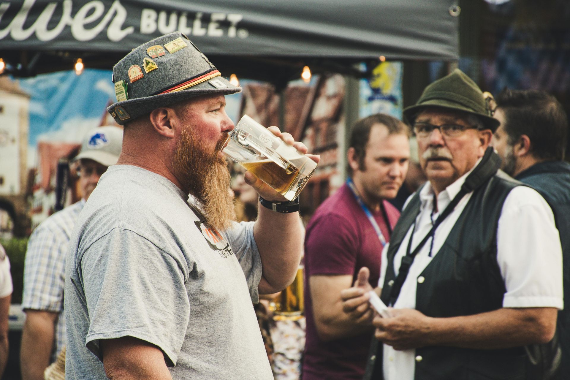 A man with a beard is drinking a glass of beer at a festival.