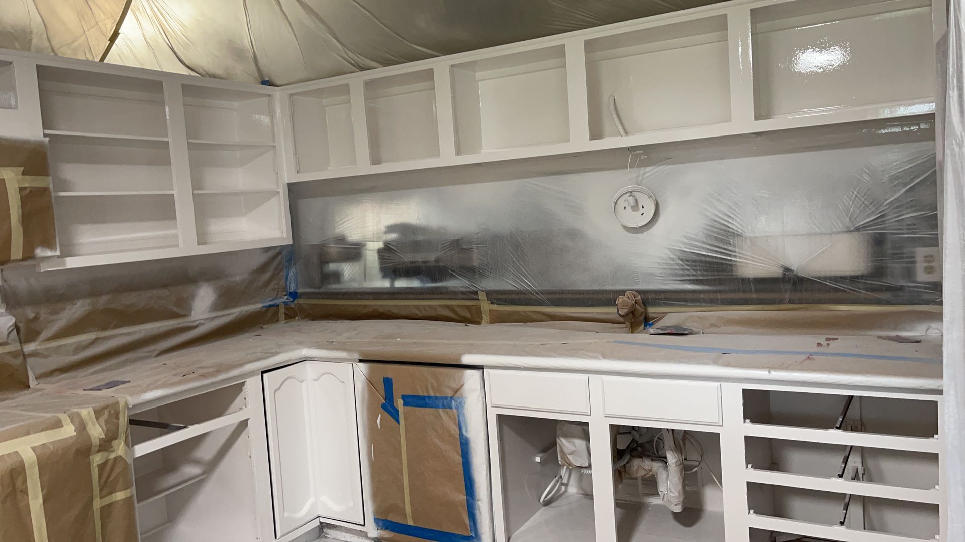 White painted kitchen cabinets, counter, and backsplash covered with plastic.