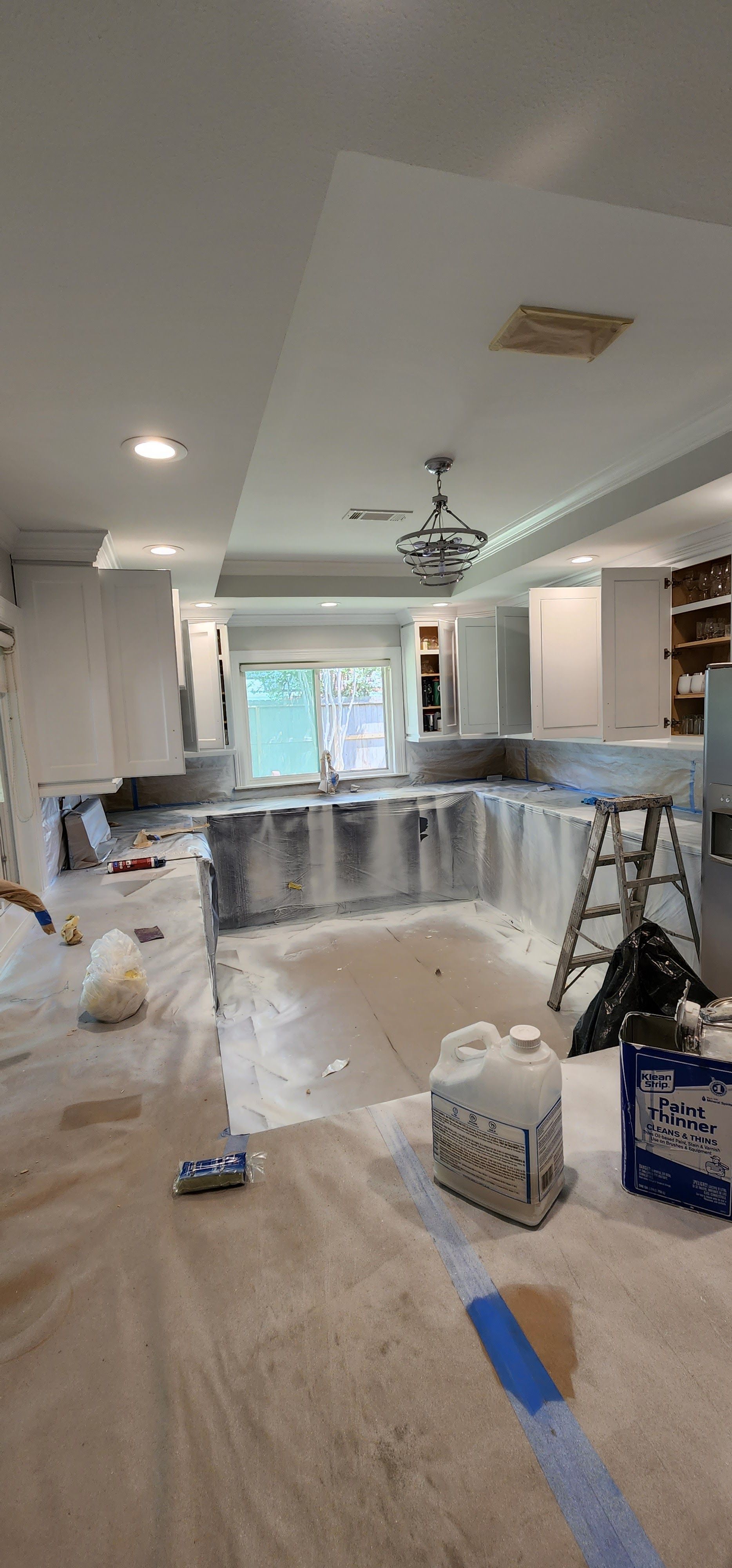 Kitchen renovation in progress: cabinets, countertops, and flooring covered in protective material.