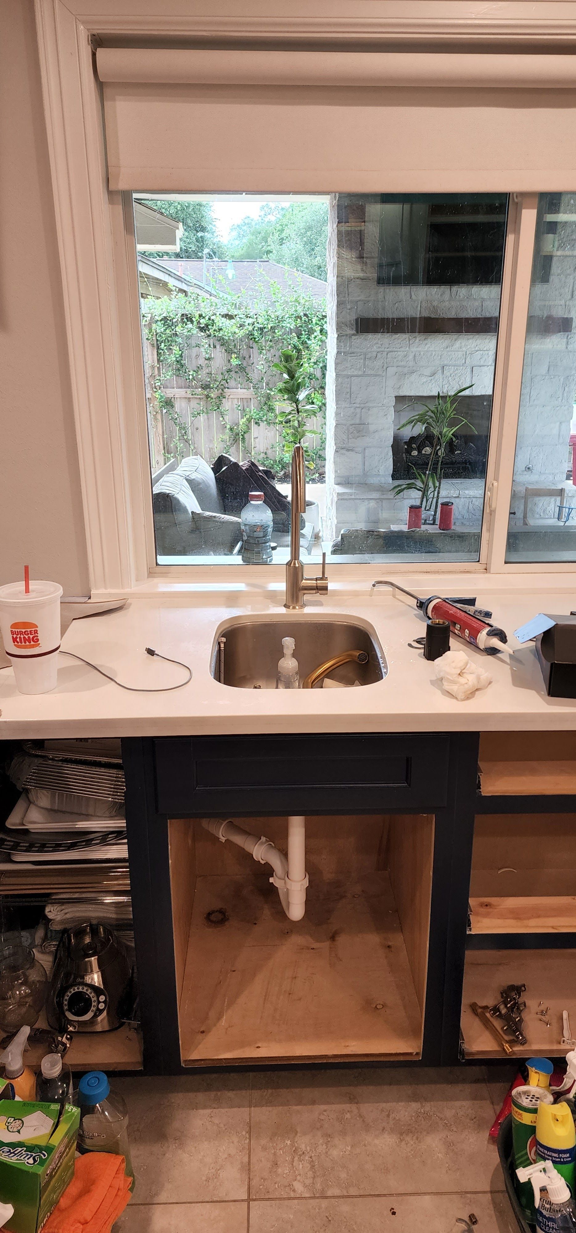 Kitchen sink installed in navy blue cabinet with unfinished interior; window view of backyard.