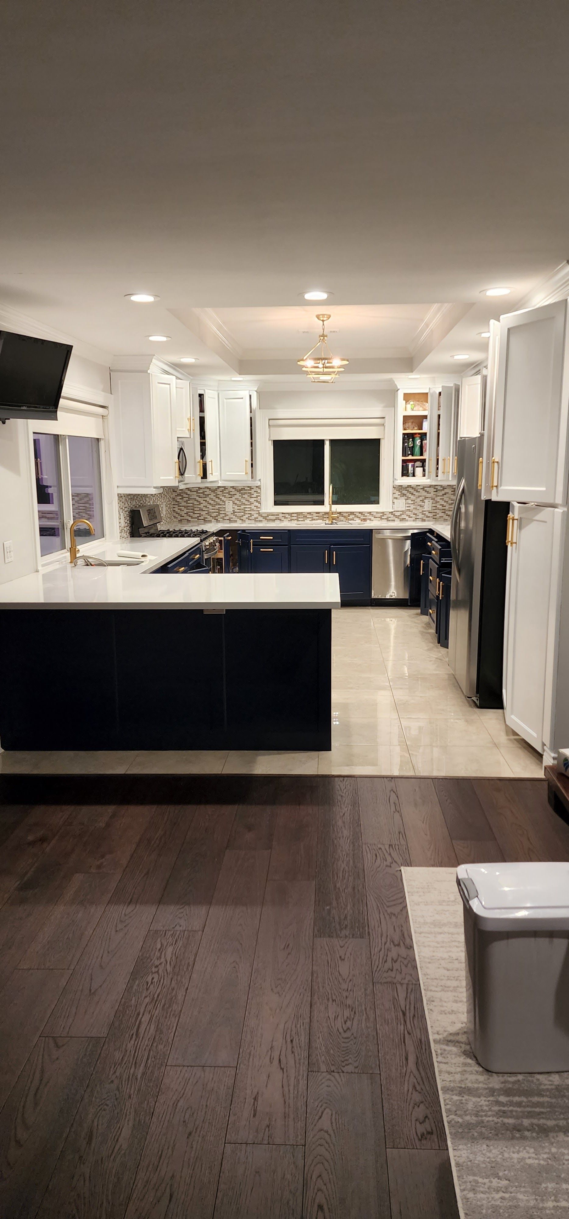 A modern kitchen with dark blue island, white cabinets, and wooden floors.