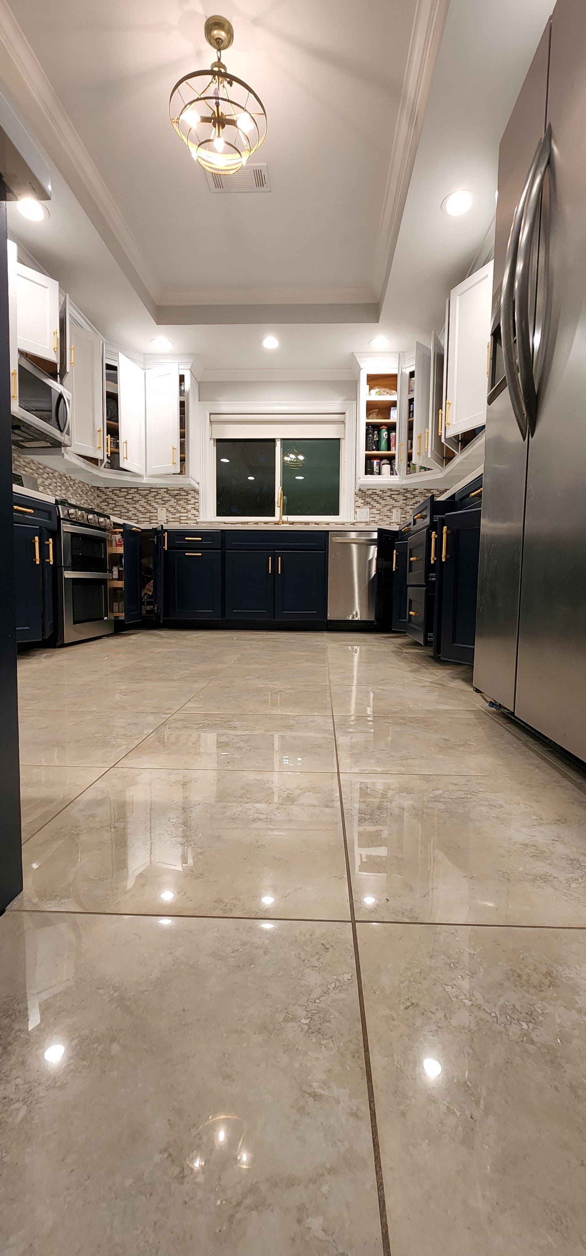 Long, narrow modern kitchen with glossy floor, dark cabinets, and a window at the far end.