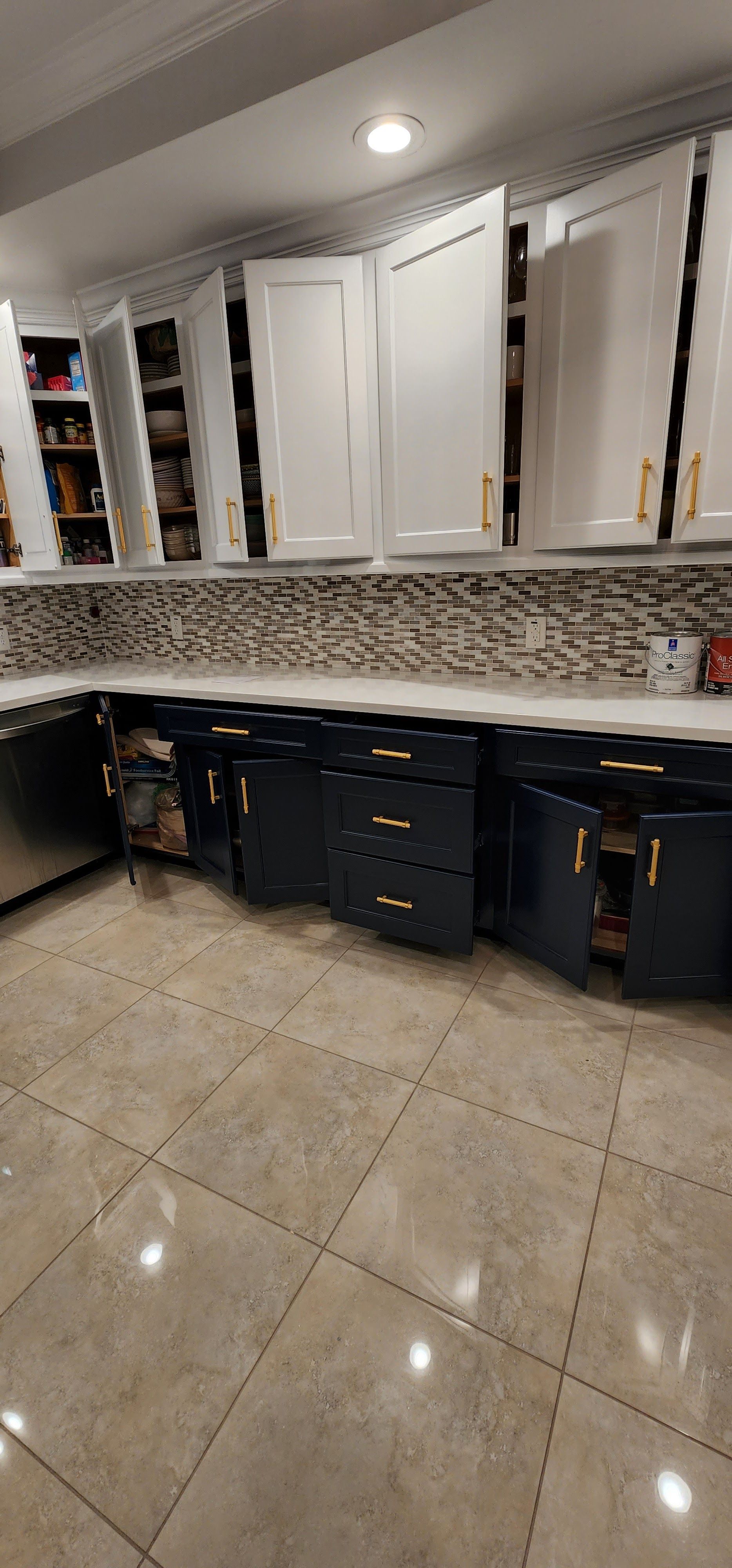 Kitchen with blue and white cabinets, open doors, and tiled backsplash.