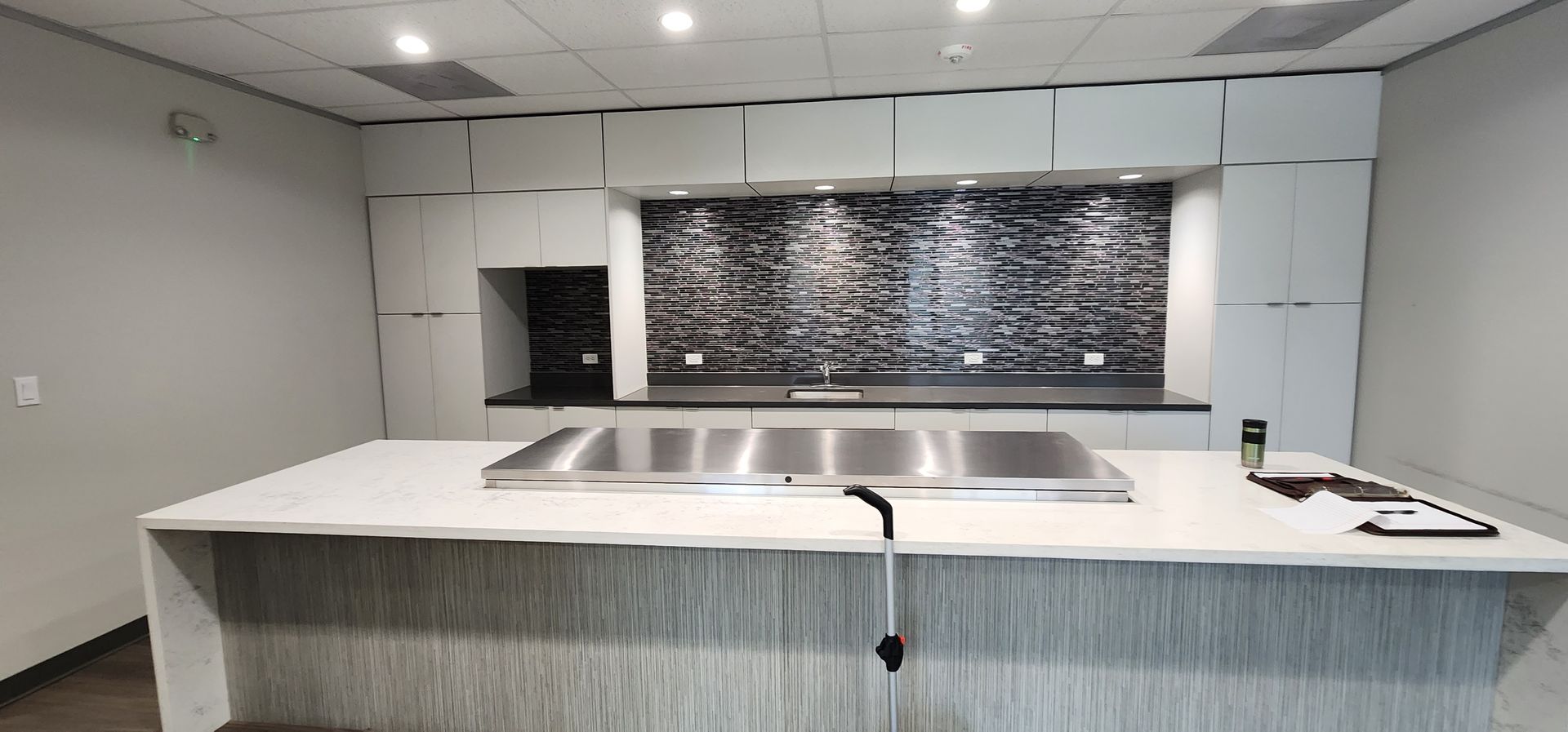 Modern kitchen with a white island and stainless steel cooktop. Dark backsplash and cabinets.
