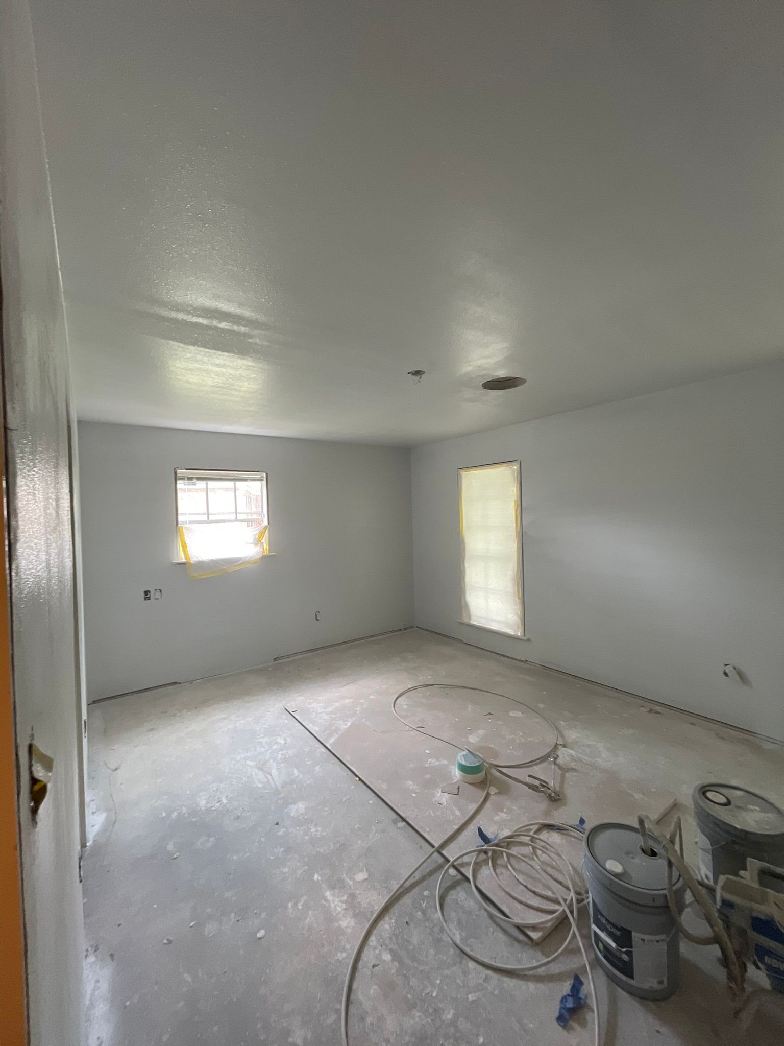 Room with freshly painted walls and ceiling; floor is unfinished. Two windows, paint buckets present.