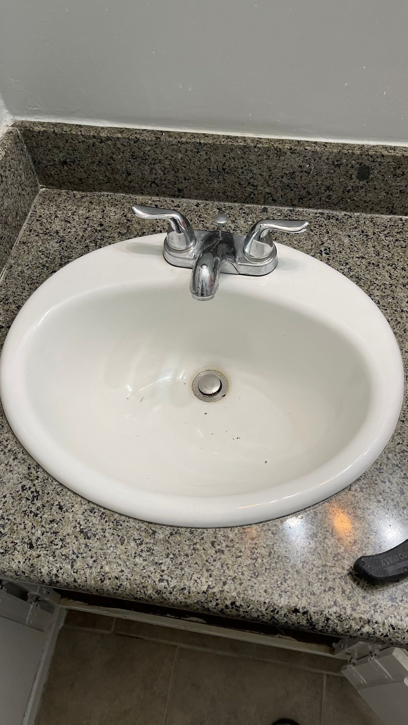 White oval bathroom sink with chrome faucet on a granite countertop.