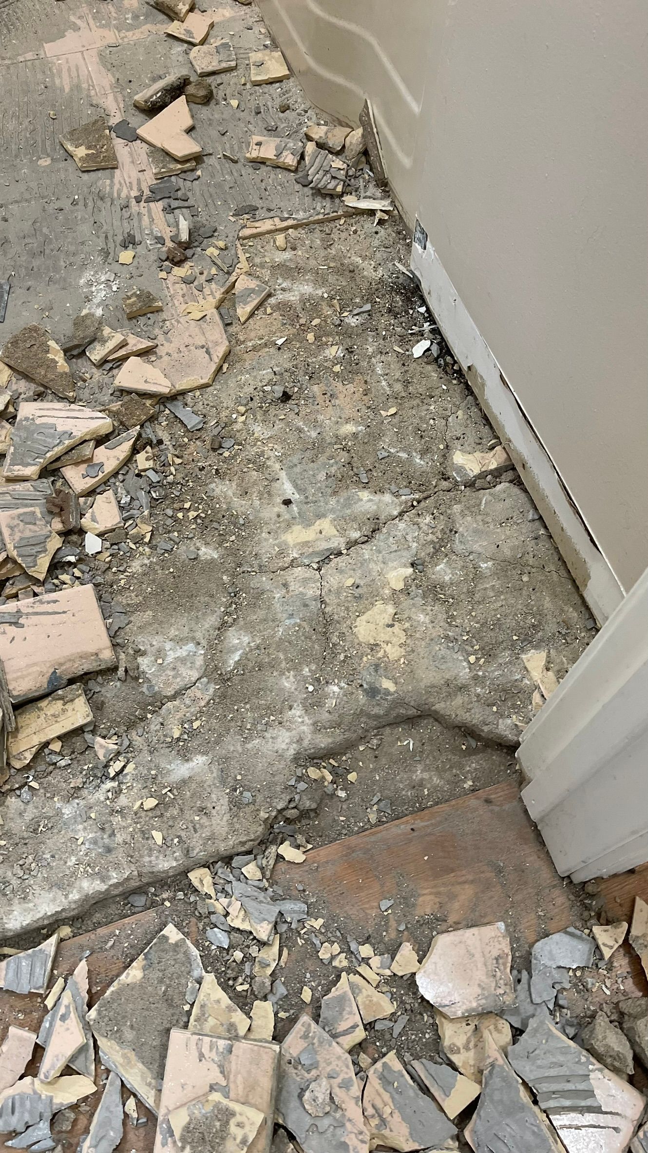 Demolished flooring with debris and exposed subfloor next to a white door frame.