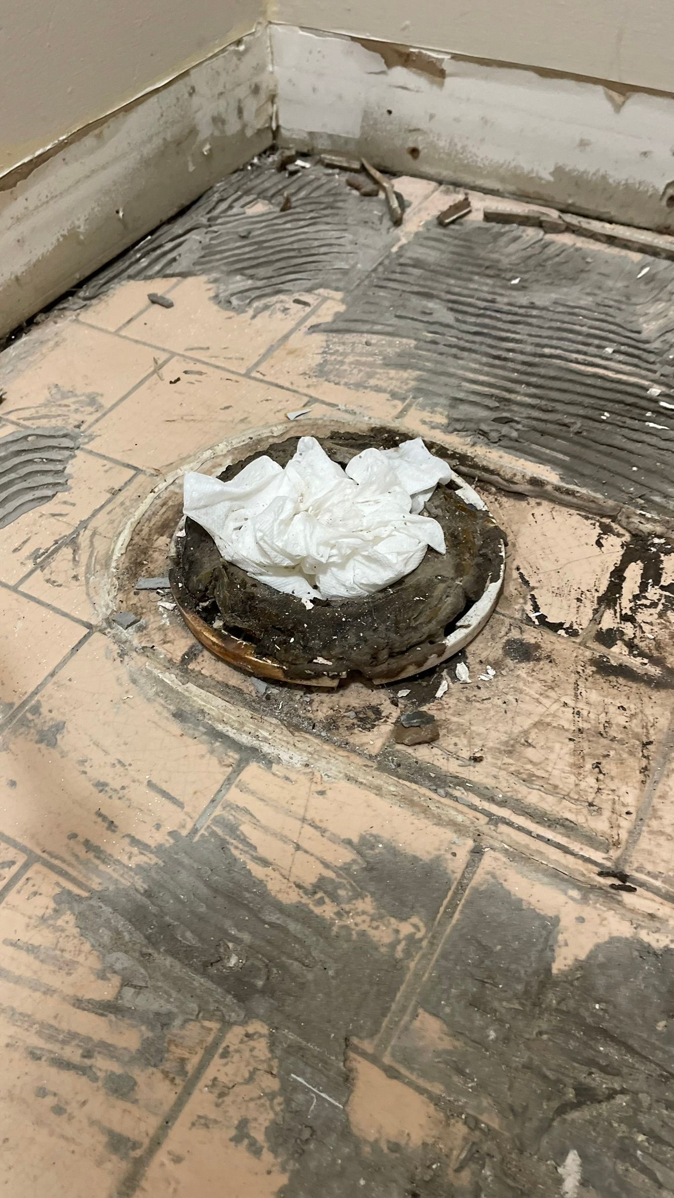 Toilet flange in a bathroom floor, covered in white paper, surrounded by damaged tile.