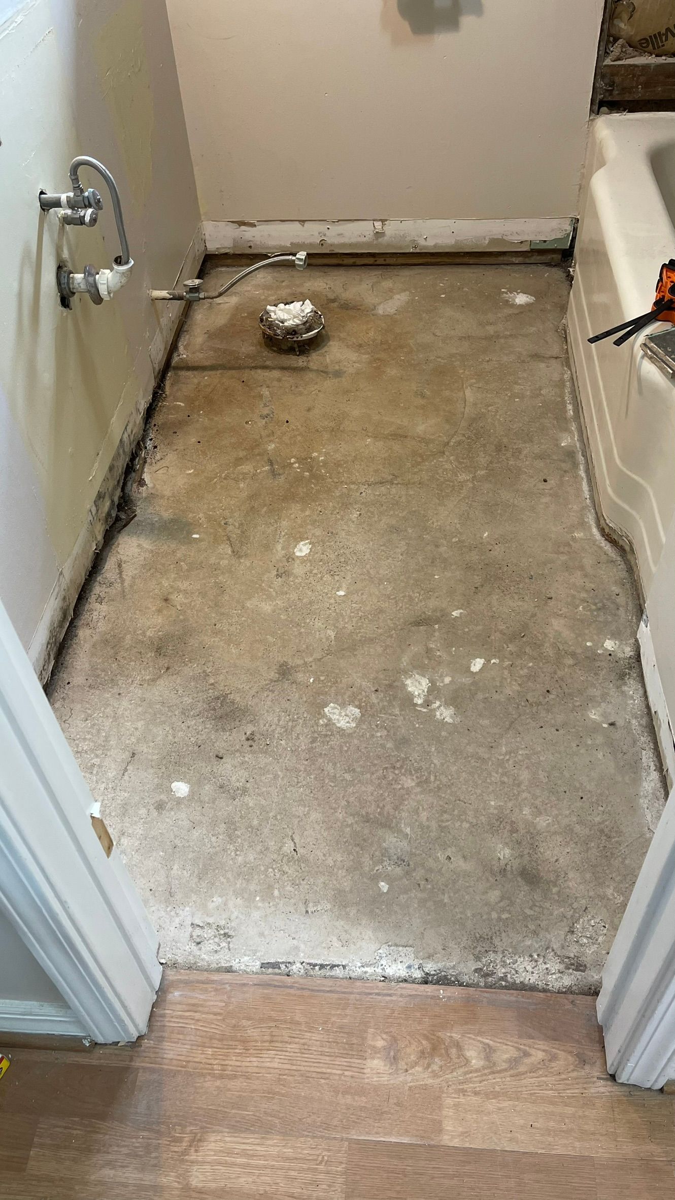 Bathroom floor in a state of renovation, with concrete and exposed pipes, and a bathtub visible on the right.