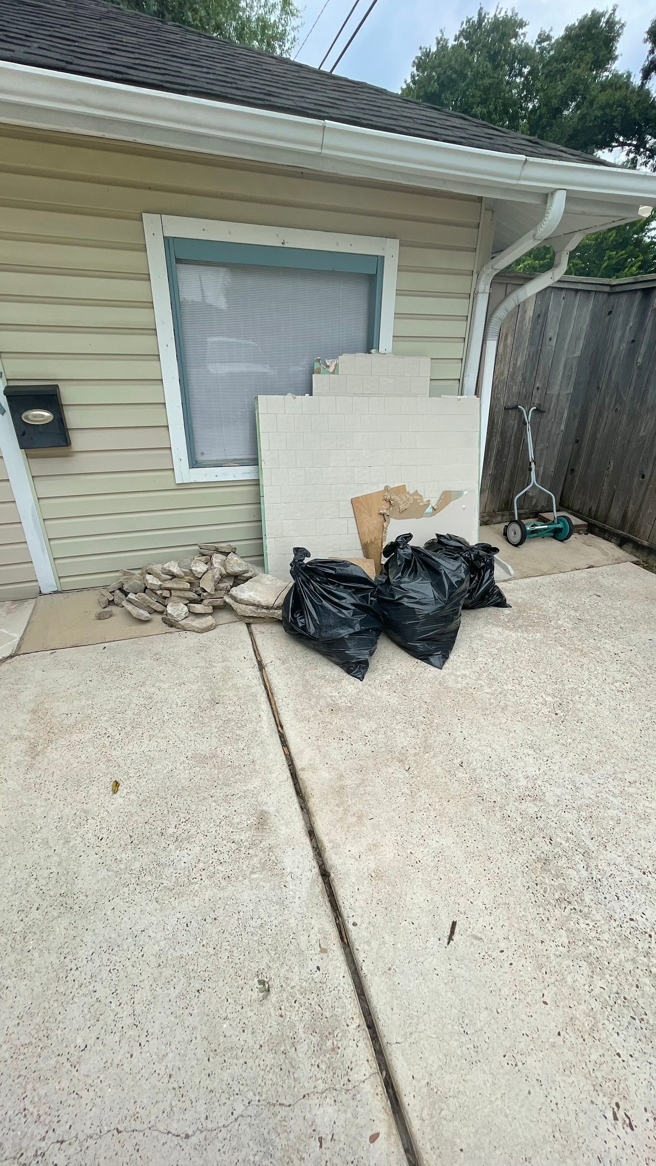 Backyard with debris, bags of trash, and a building with a window.