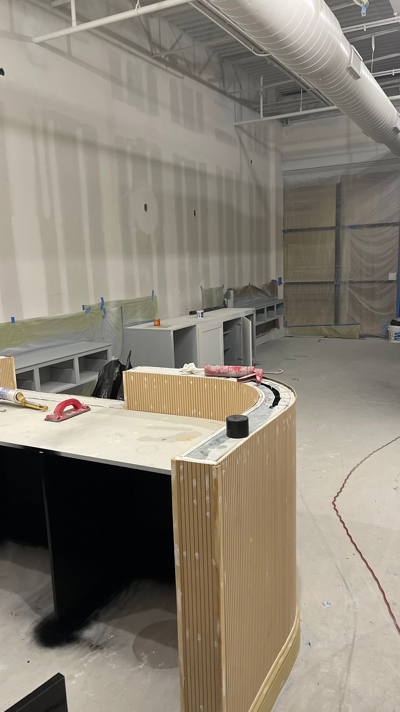 Construction site with unfinished walls and a curved wood desk; various tools and building materials visible.