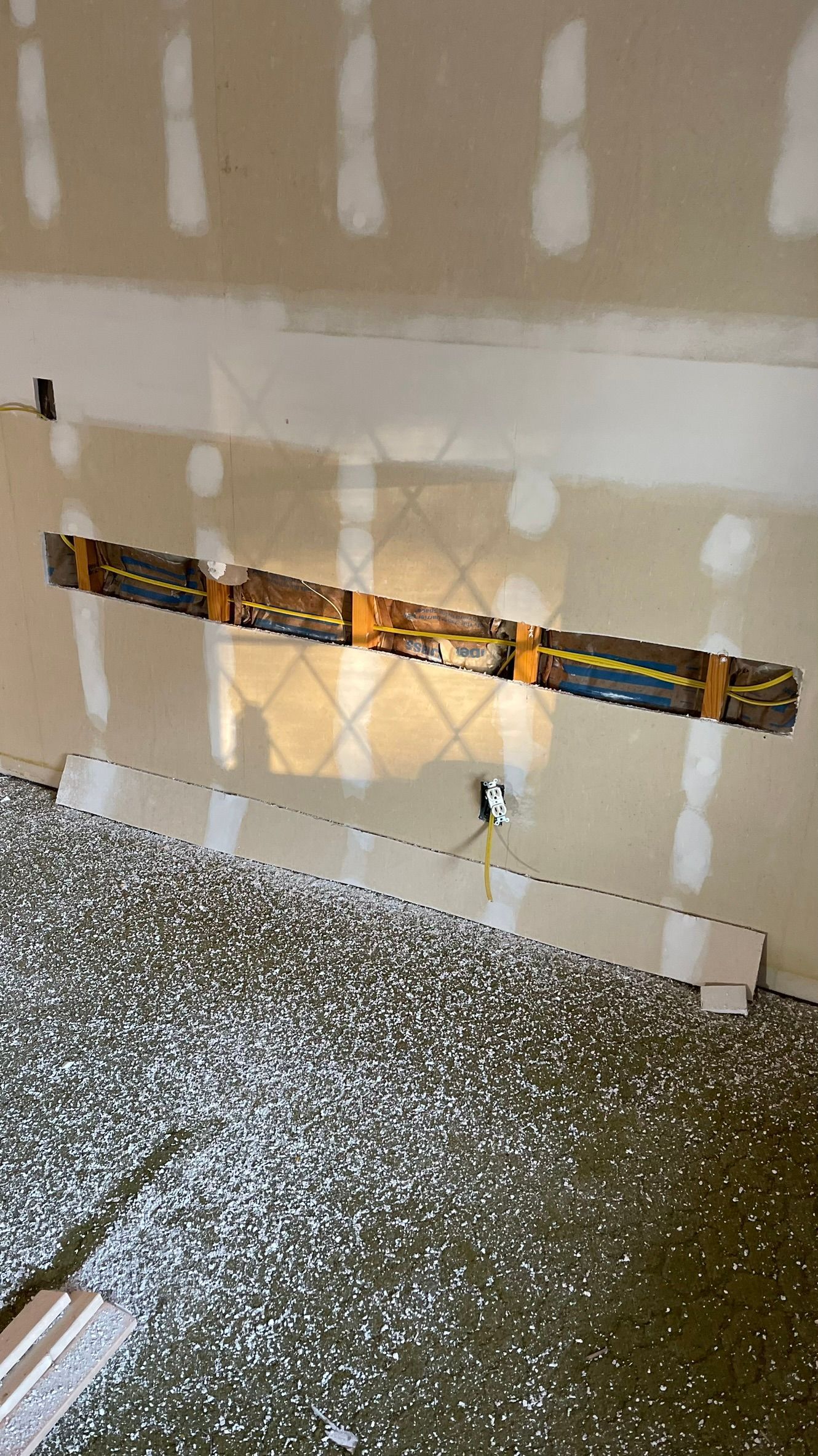 Electrical wiring and conduit secured within a wall opening above a gravel floor.