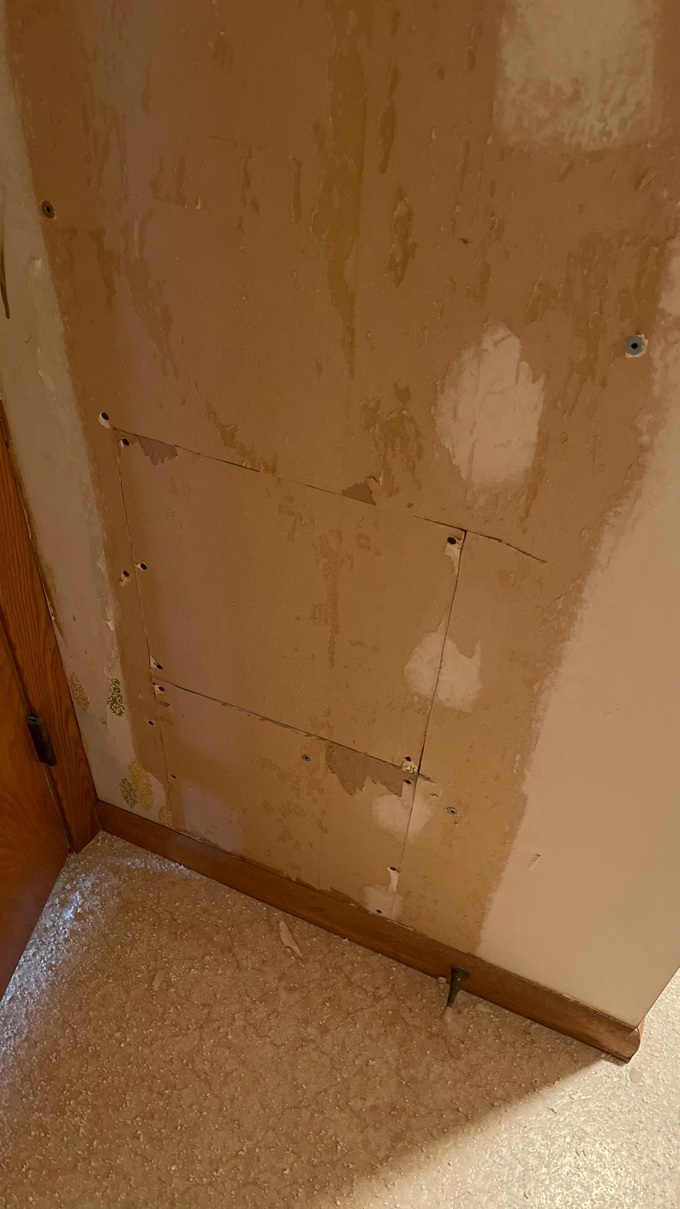 Wall with exposed drywall, screw holes, and patches of paint, near a carpeted floor.
