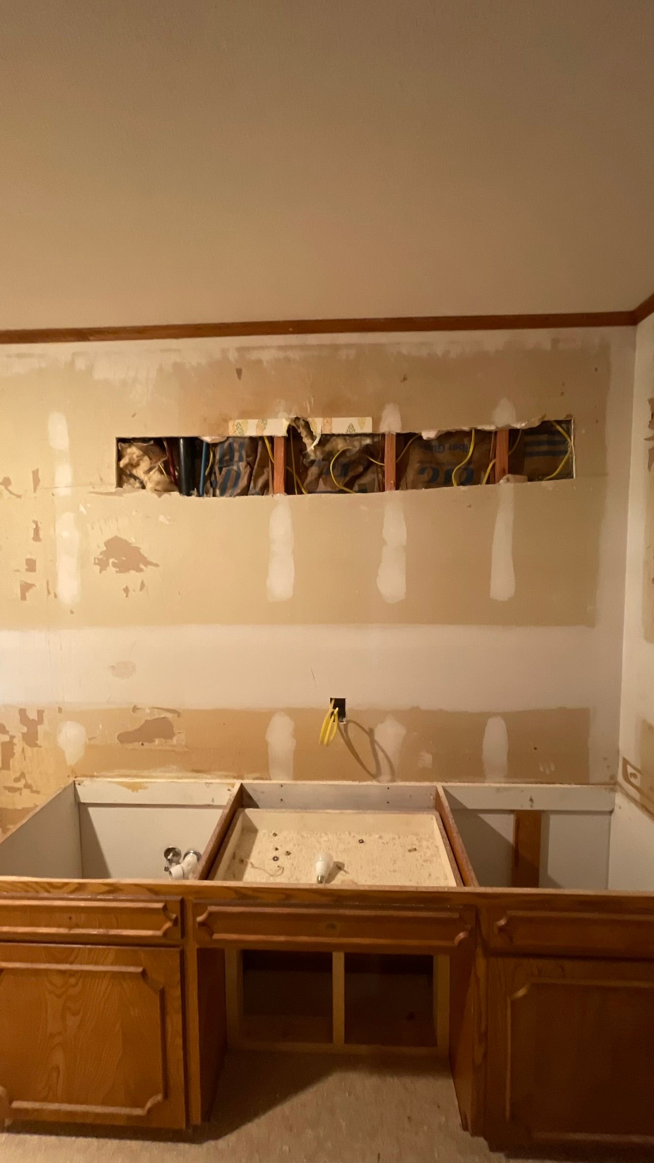 Kitchen wall with a section removed, exposing electrical wiring. Cabinets below.