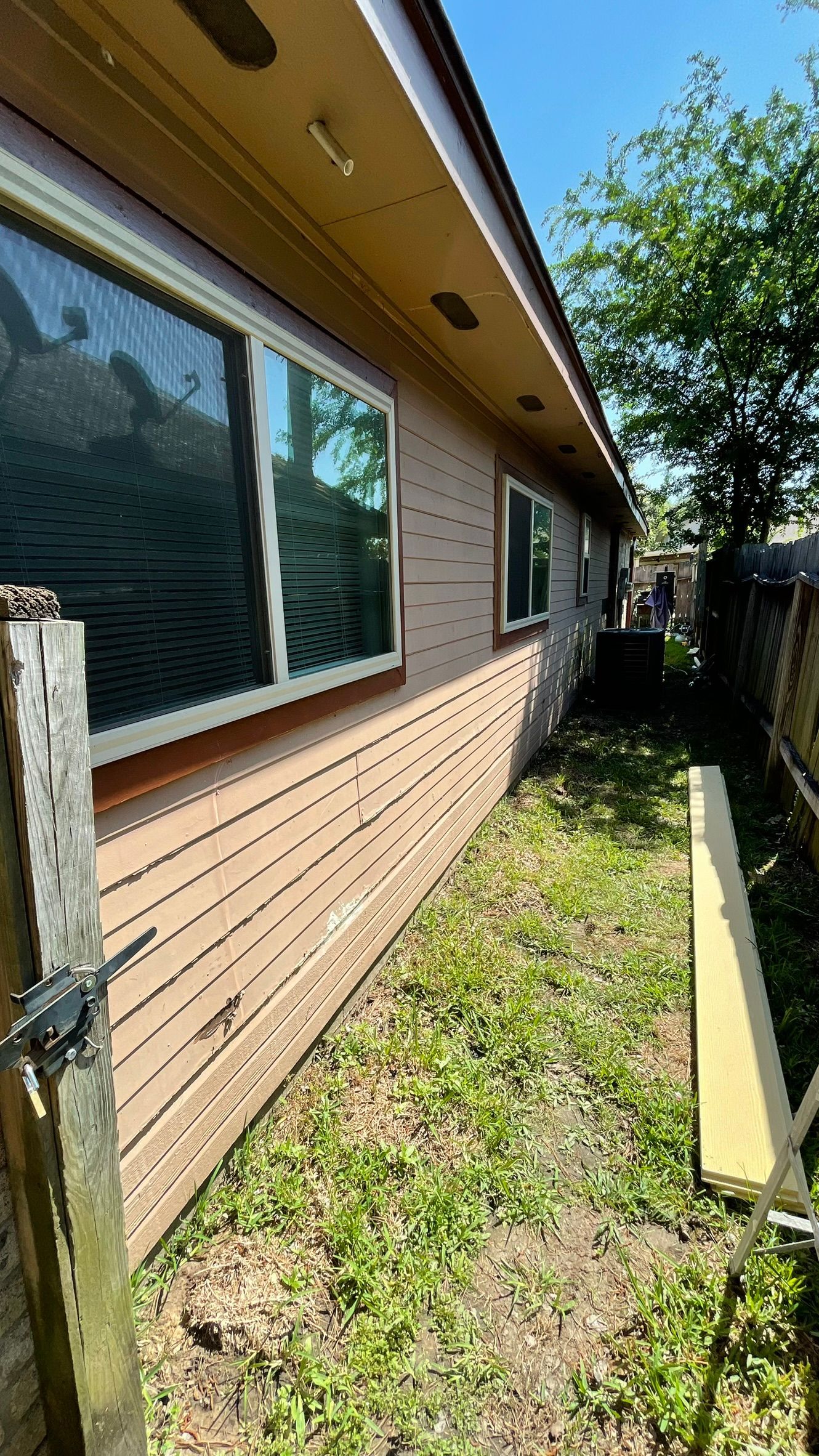 Side of a building with windows, tan siding, and narrow overgrown grass pathway.