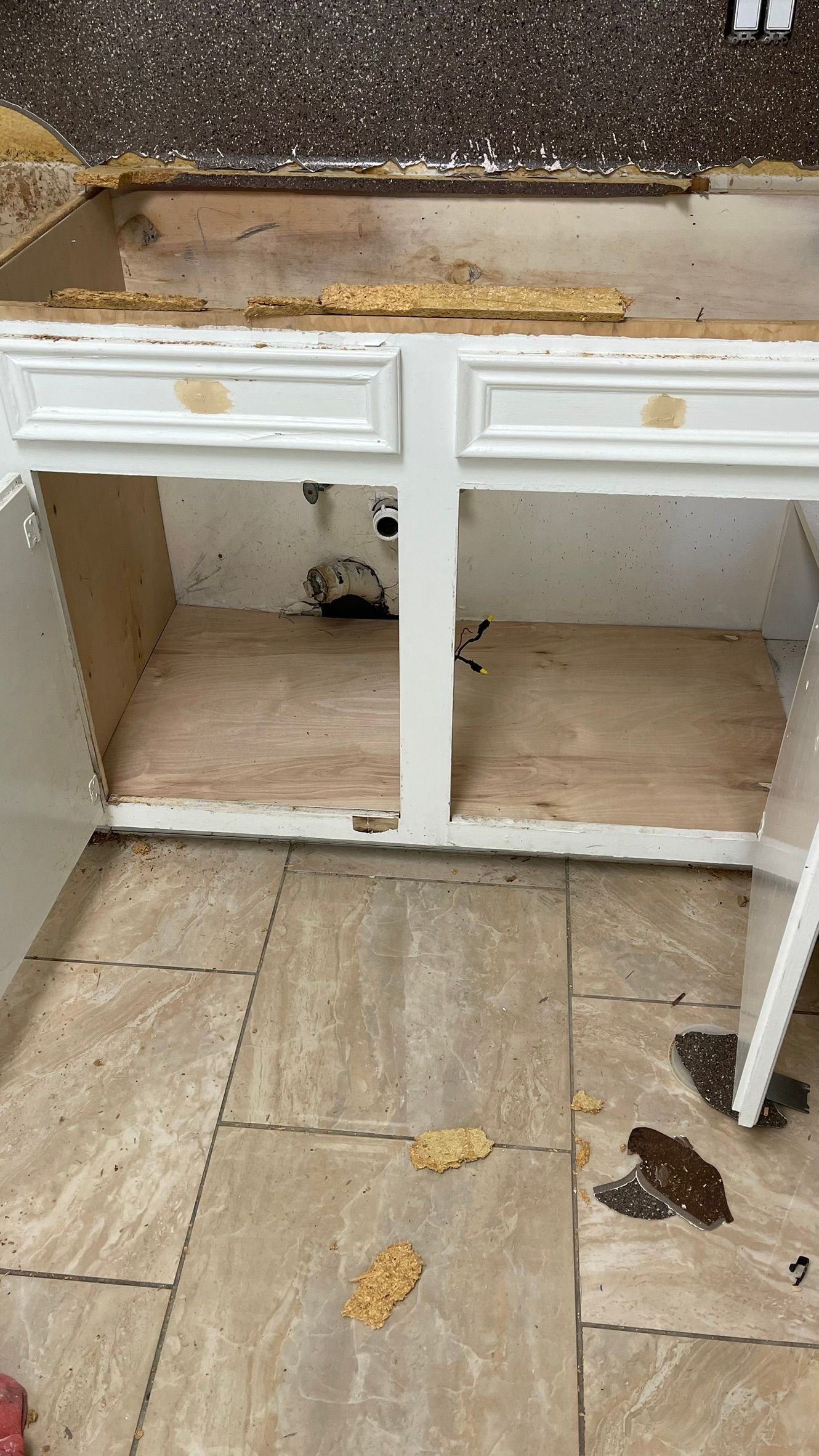 Kitchen cabinet with missing countertop, exposing inside, surrounded by debris on the floor.
