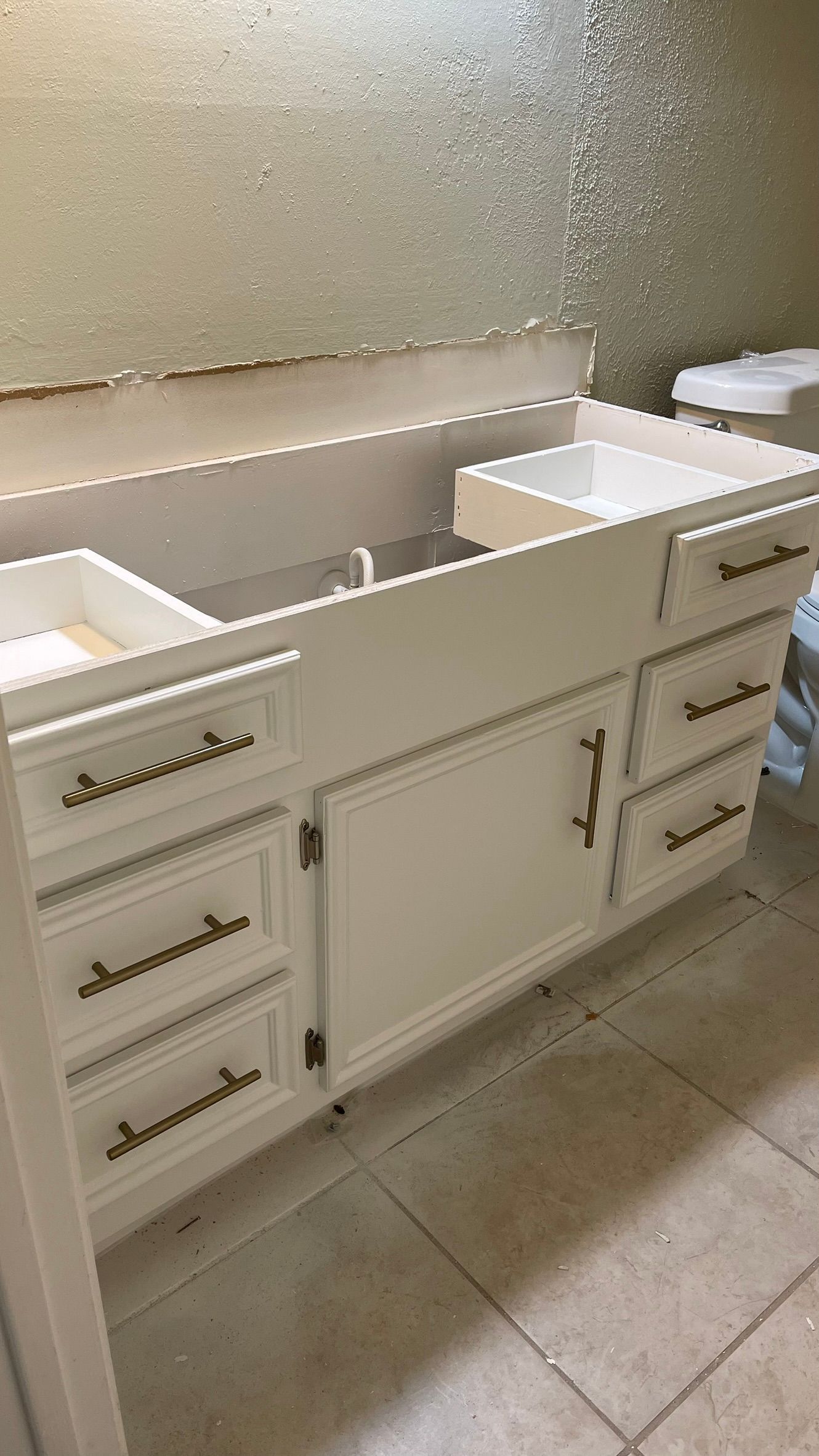 White bathroom vanity with gold hardware, drawers, and a central cabinet. Light beige backsplash.