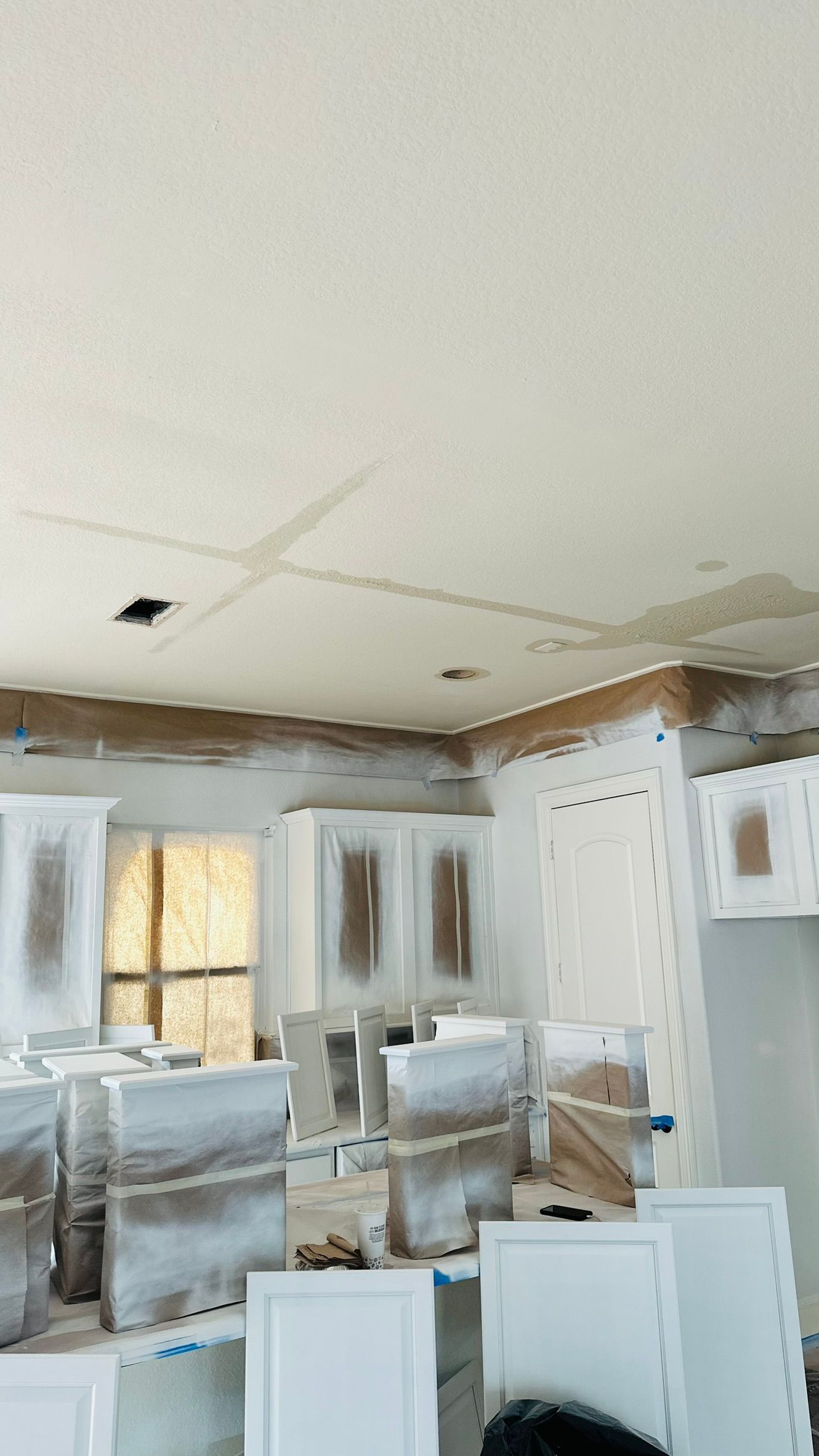 White kitchen cabinets being painted in a room with a light-colored ceiling and a window.
