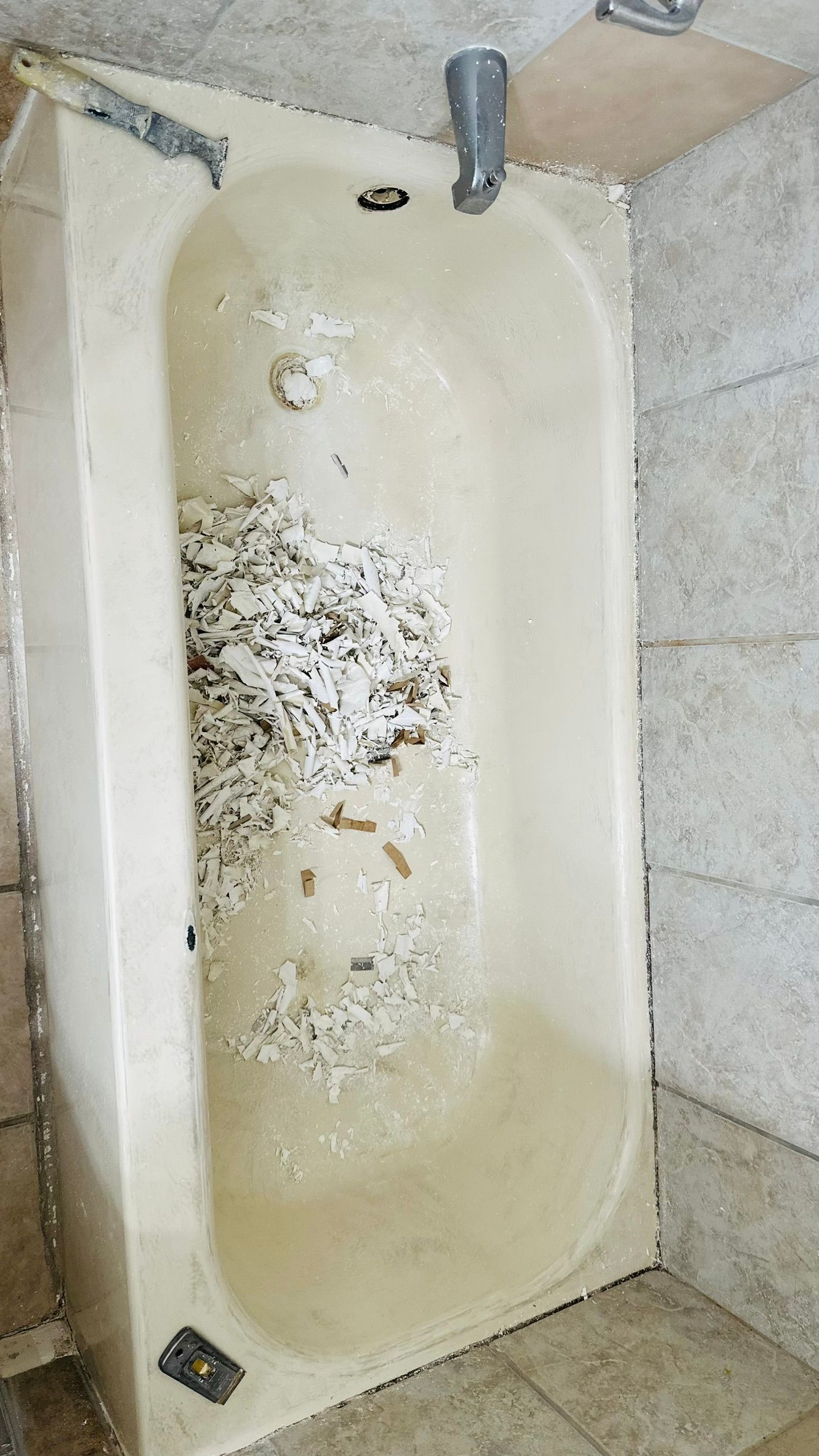 A dirty, off-white bathtub filled with debris, viewed from above, between tiled walls.