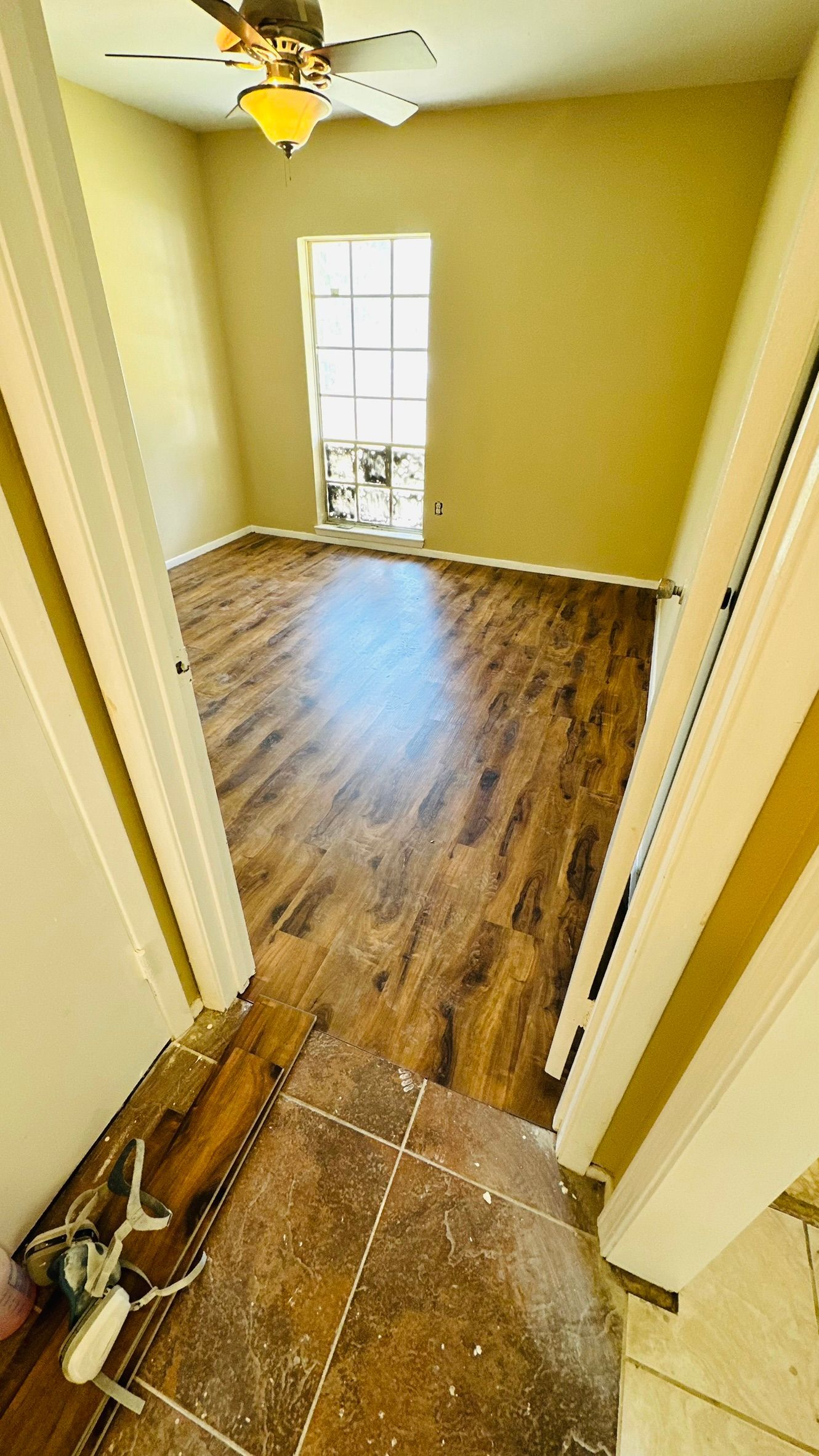 Room with brown hardwood floors, tan walls, and a window. Light from window illuminates the room.