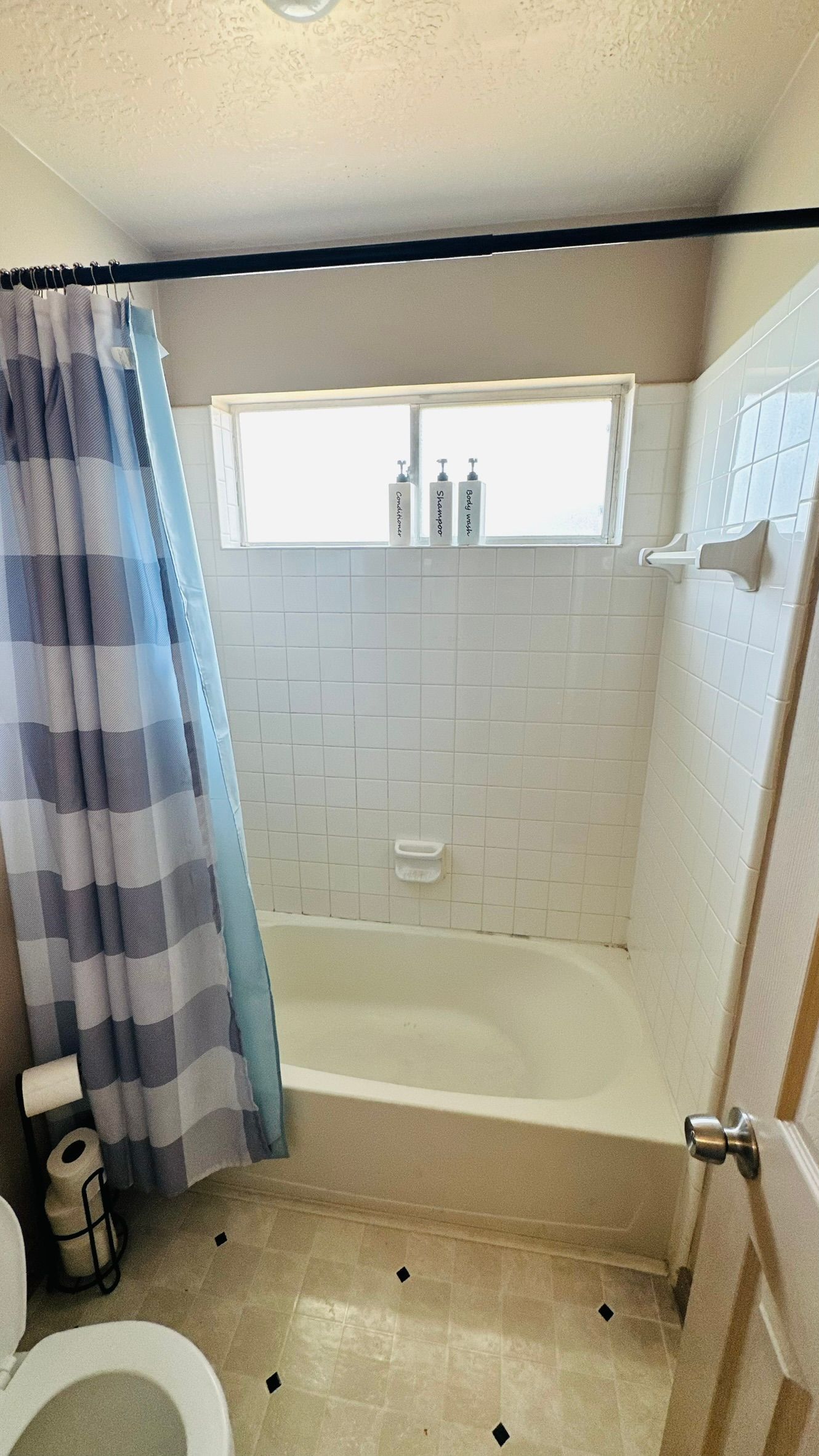 Bathroom with a white bathtub, white tiled walls, and a blue and white striped shower curtain.