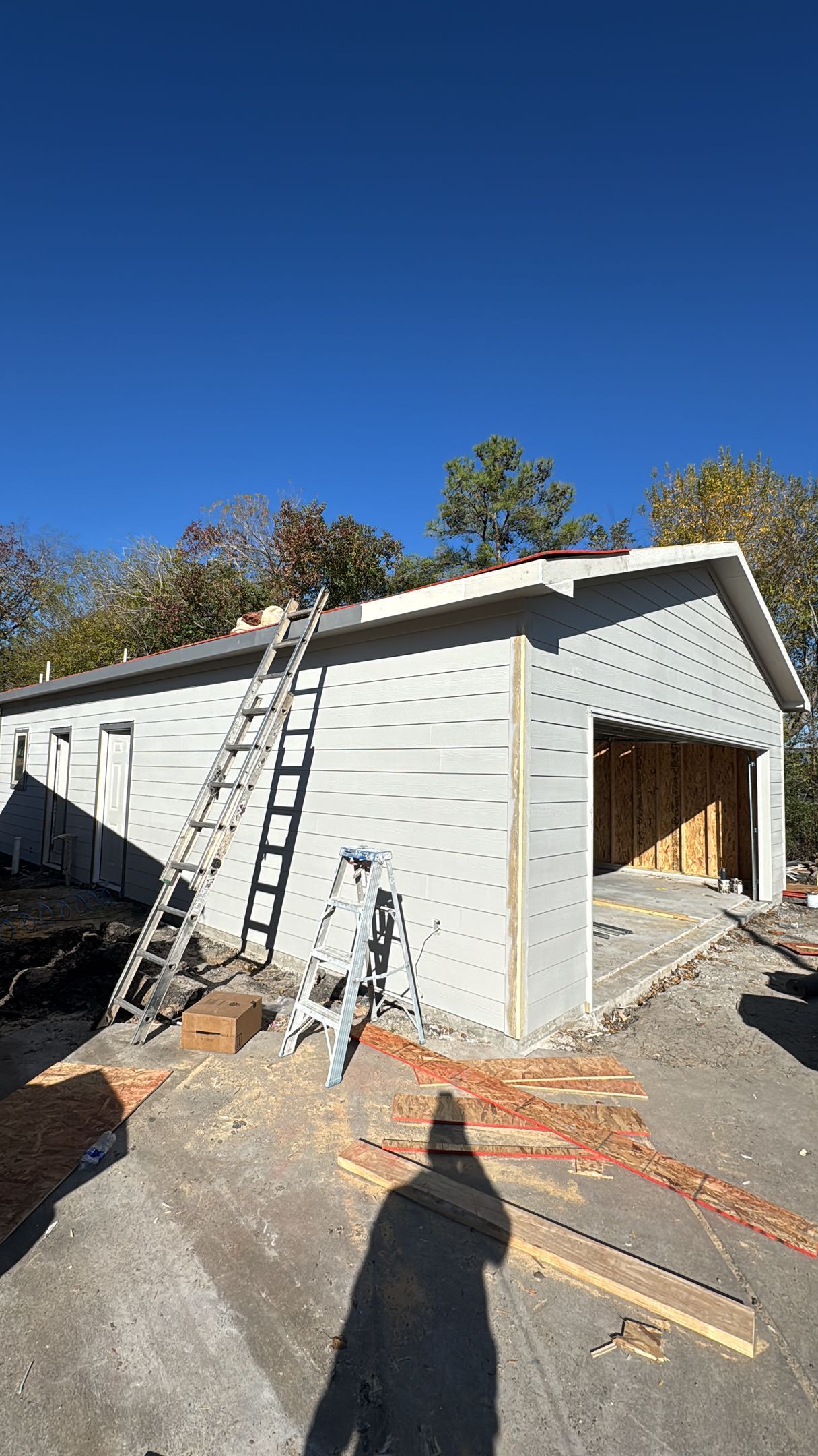 Garage under construction with a ladder against the side, against a blue sky.