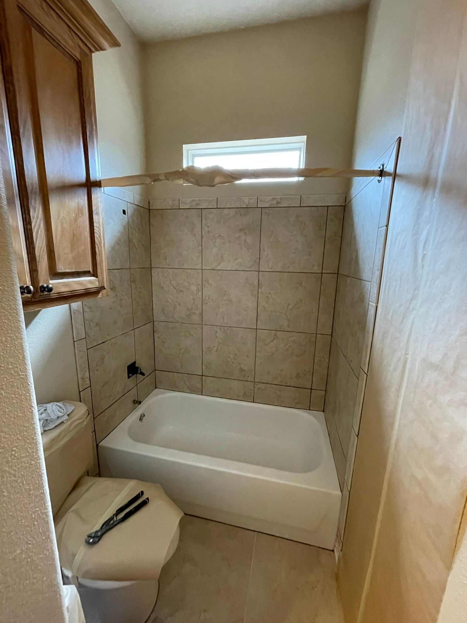 Small bathroom with a tub, toilet, and tiled walls. A wood support is across the tiled area.