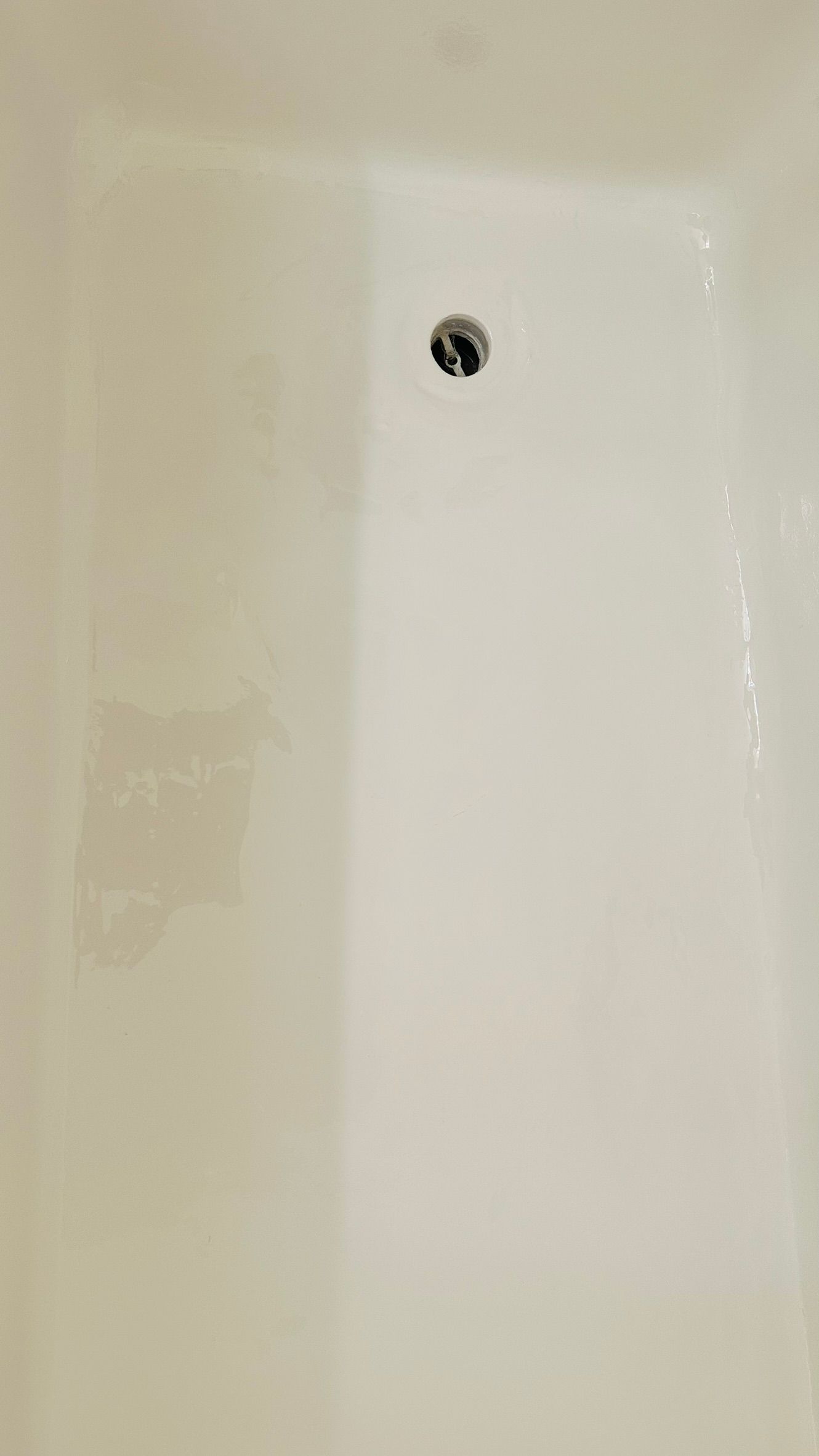 White bathtub with drain in the center, wet surface.