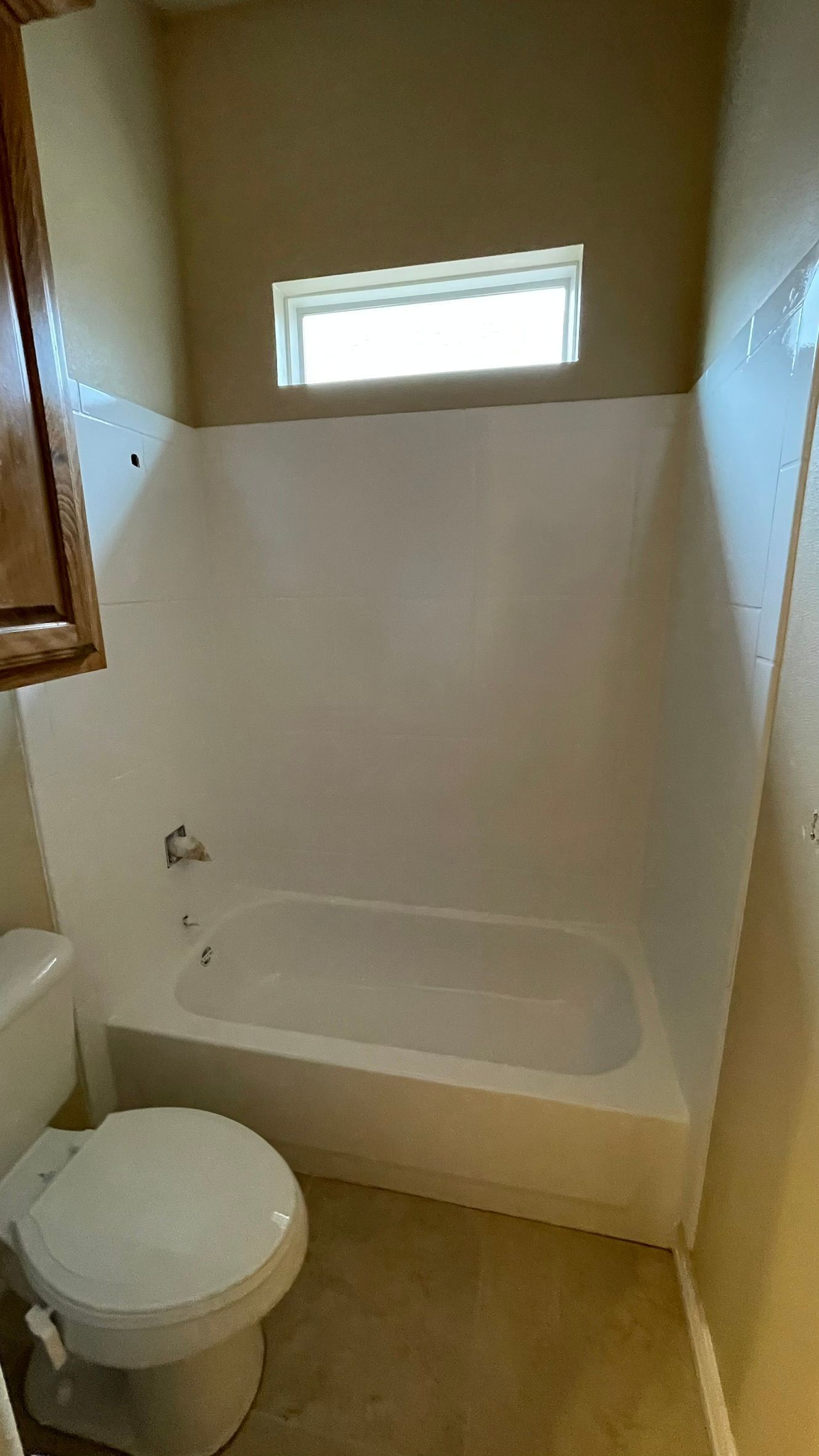 Small bathroom with a white bathtub, toilet, and a small window.