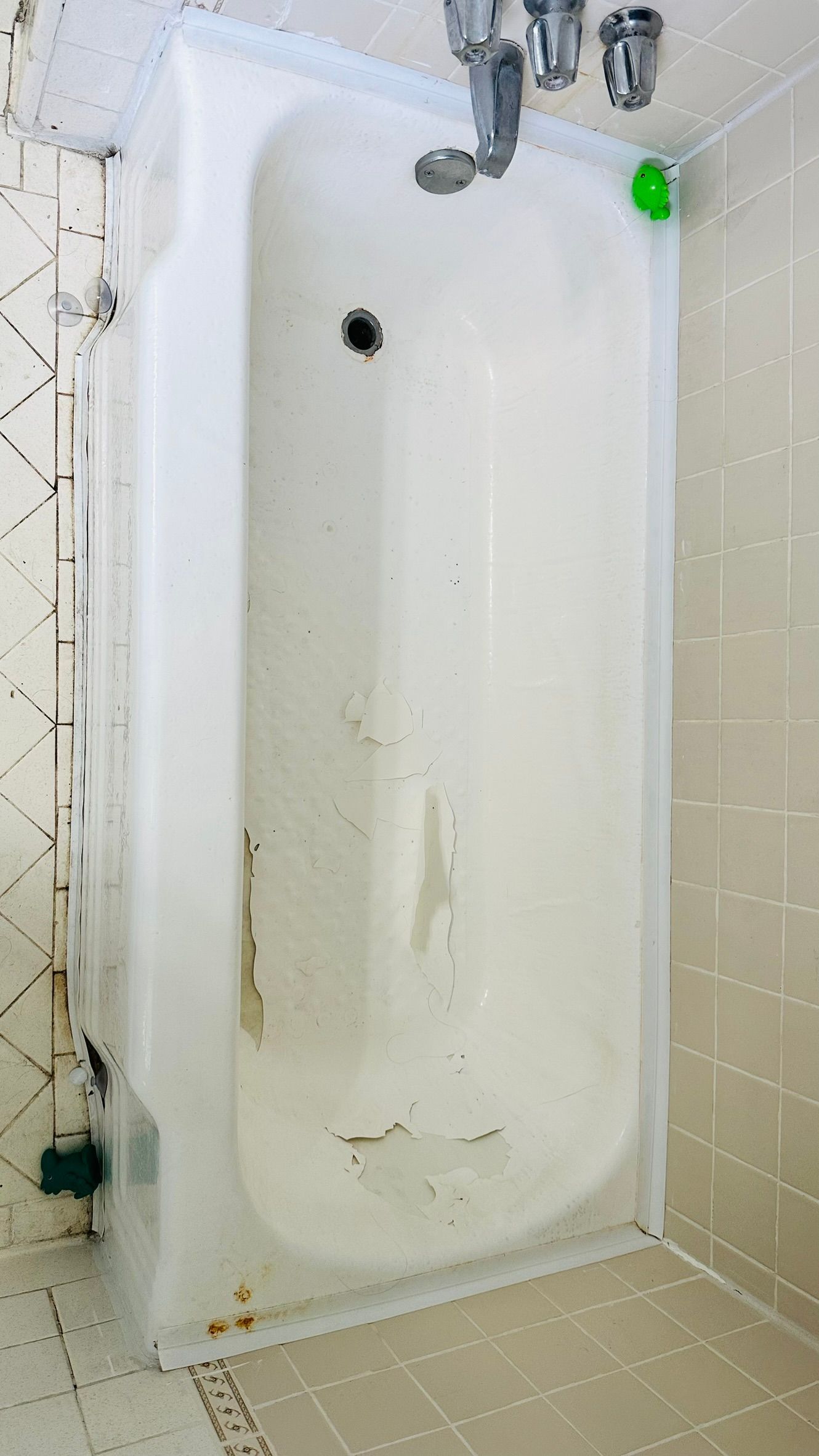 White bathtub with peeling surface and rust stains in a tiled bathroom.
