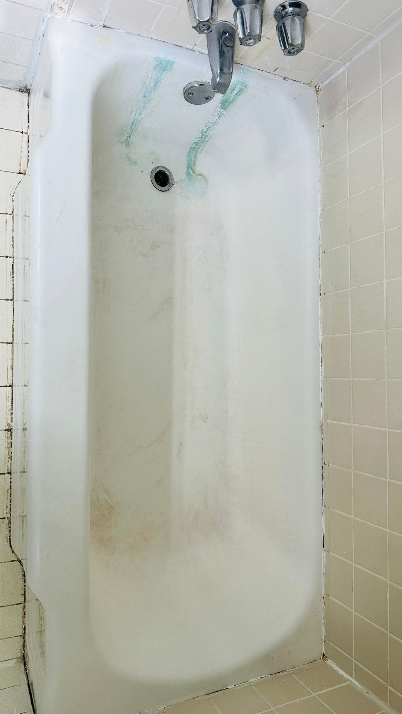 White bathtub with shower head and faucet. Tile surround with some mildew.
