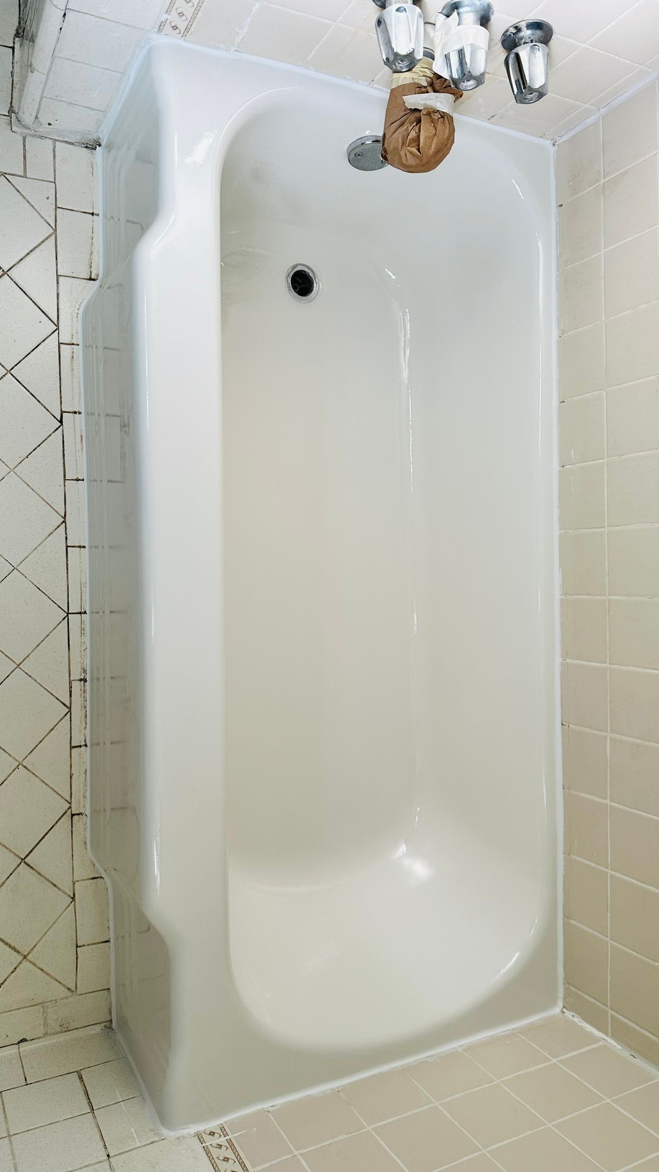 White bathtub in a tiled bathroom, with faucets and showerhead above.