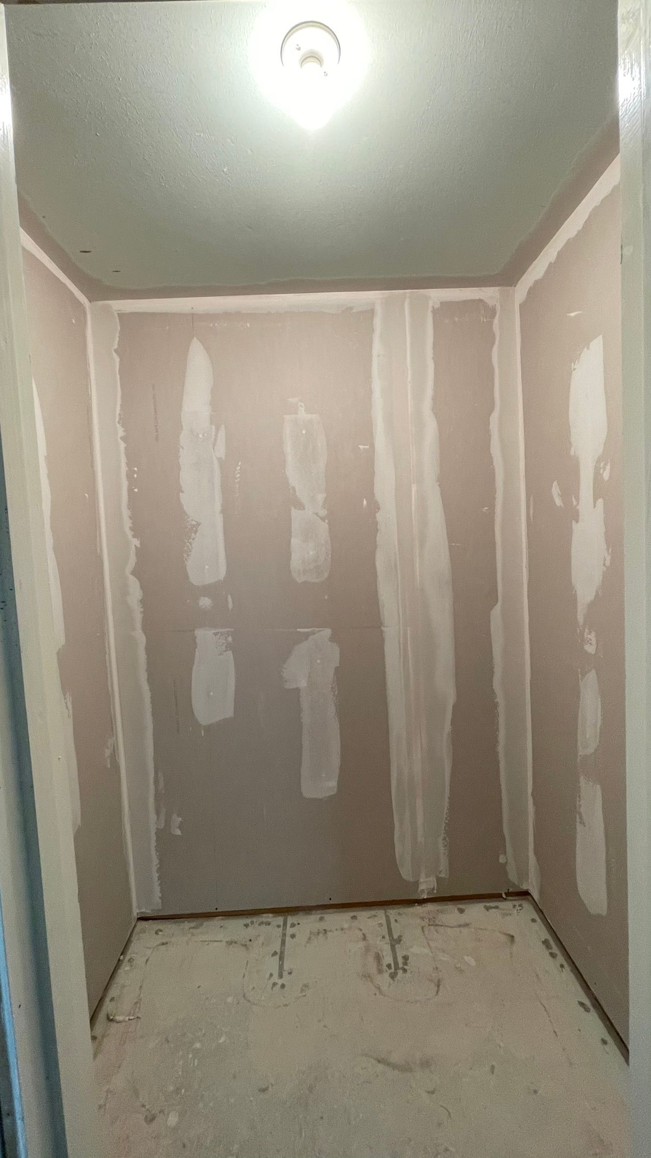 Small, unfinished room with drywall on walls and ceiling; exposed seams and white compound visible.