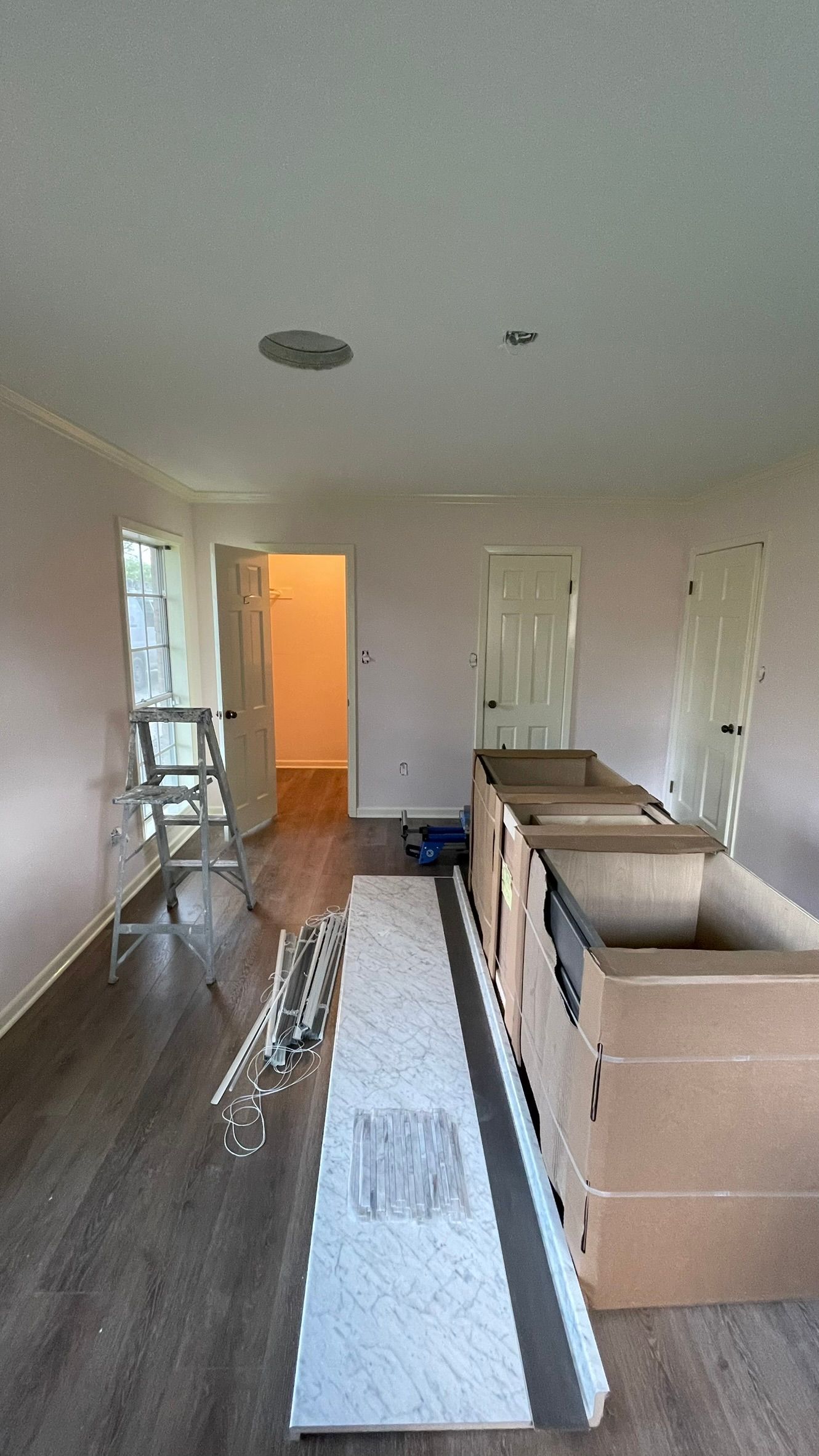 Interior shot of a room with unfinished cabinets and flooring. There's a door at the end and a stepladder.