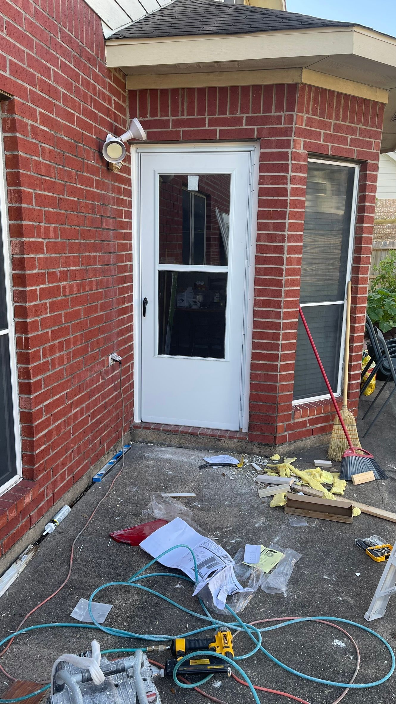 Red brick exterior with white door, construction materials scattered on the ground.