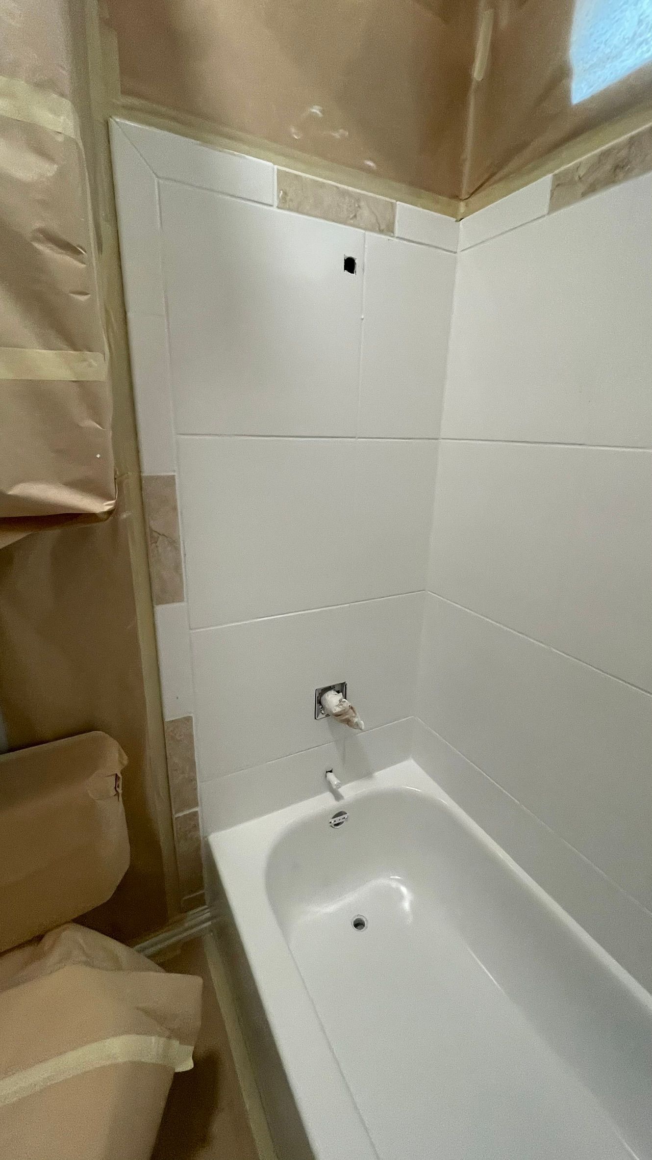 White bathtub and shower wall partially installed in a bathroom under renovation; plumbing fixtures visible.