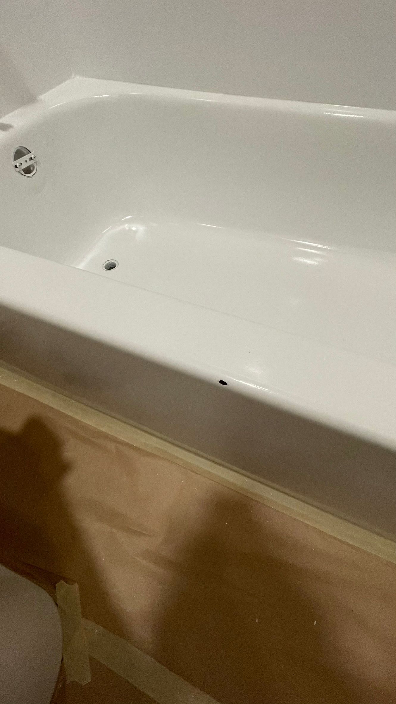 White bathtub with spouts, next to a wood-colored floor. The bathtub is clean, and the floor is protected with tape.