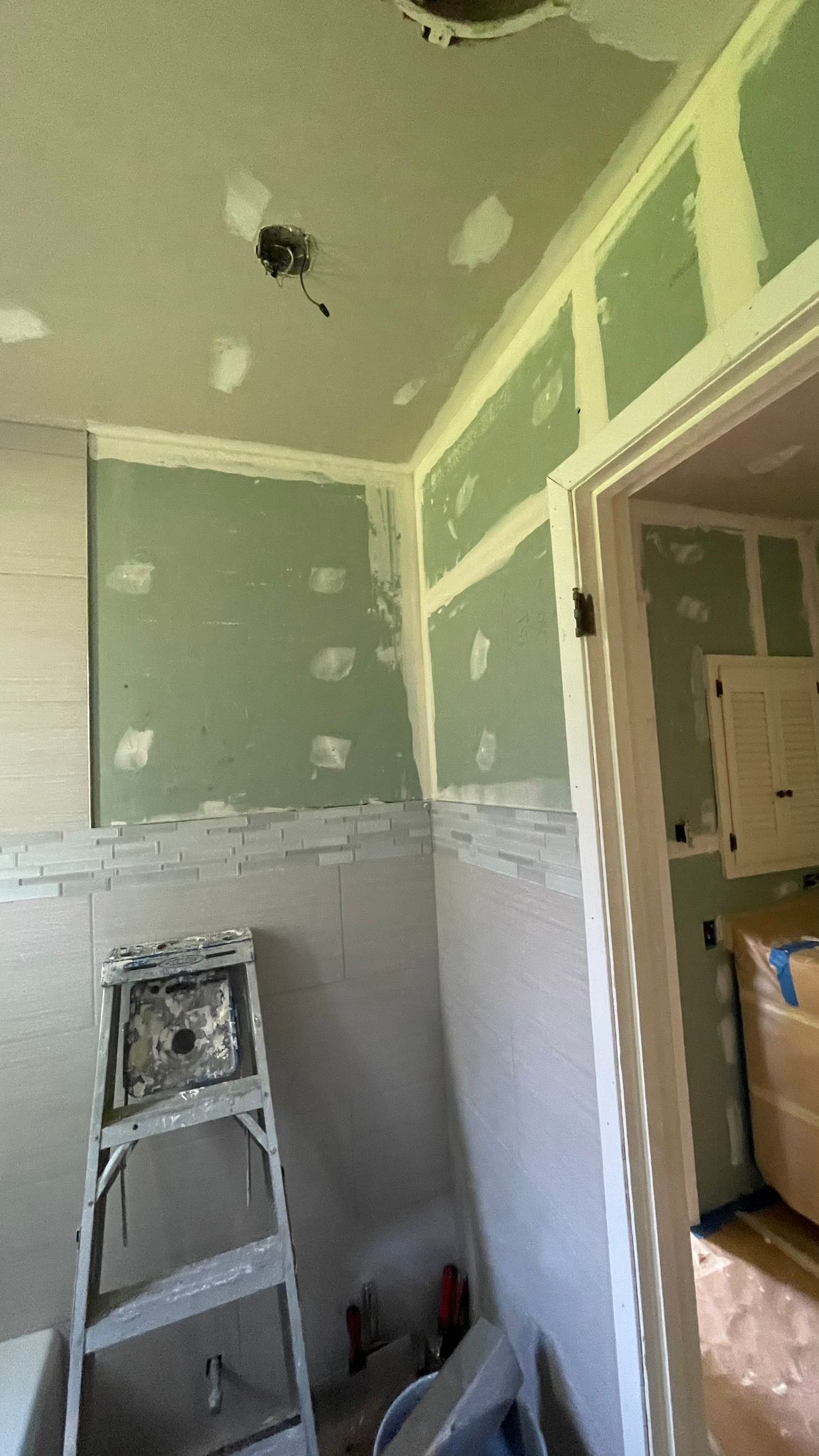 Interior view of a room under construction with green drywall, a ladder, and a doorway.