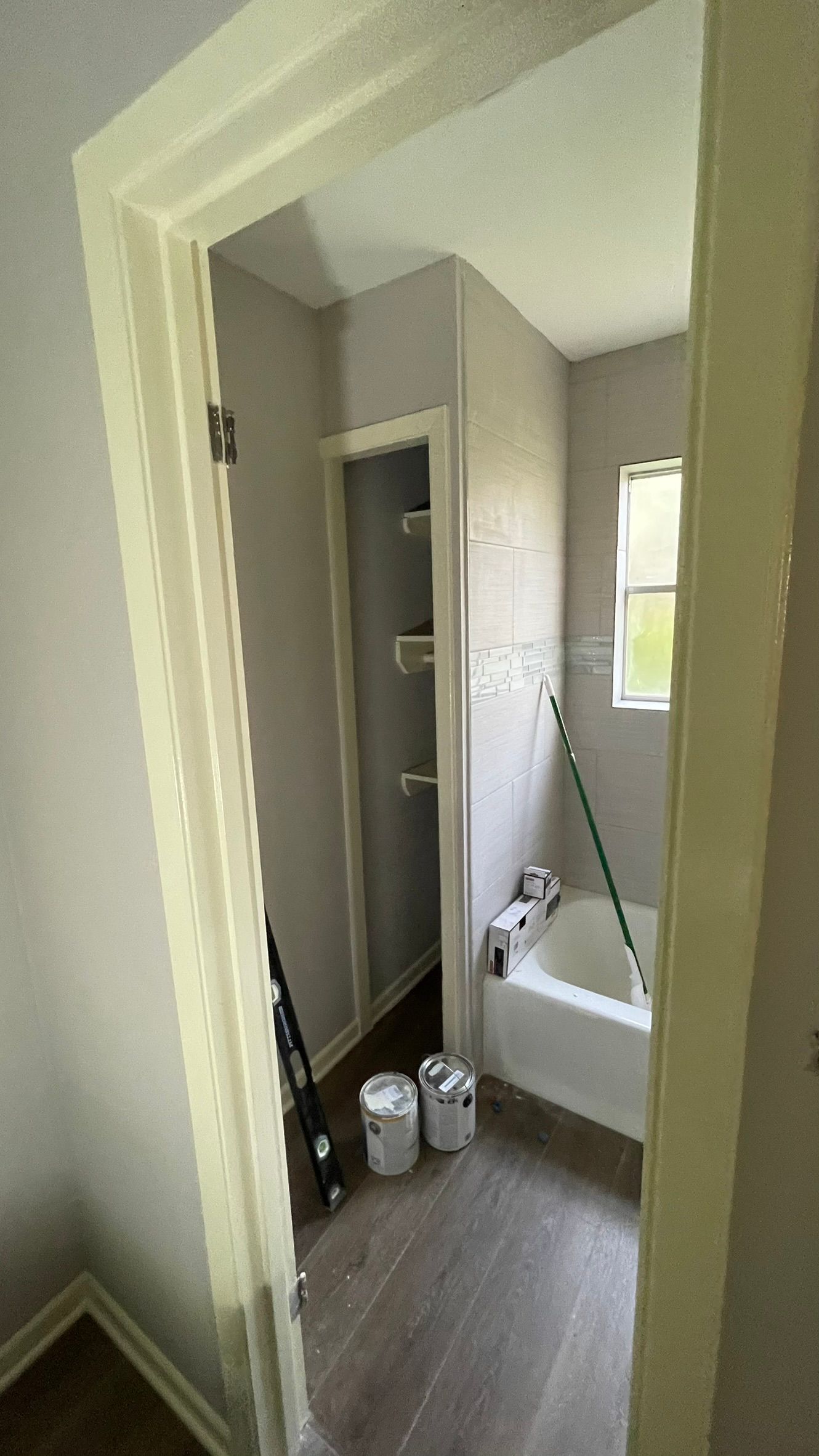 Bathroom interior with freshly painted gray walls, shelves, and a bathtub. Paint cans and tools present.