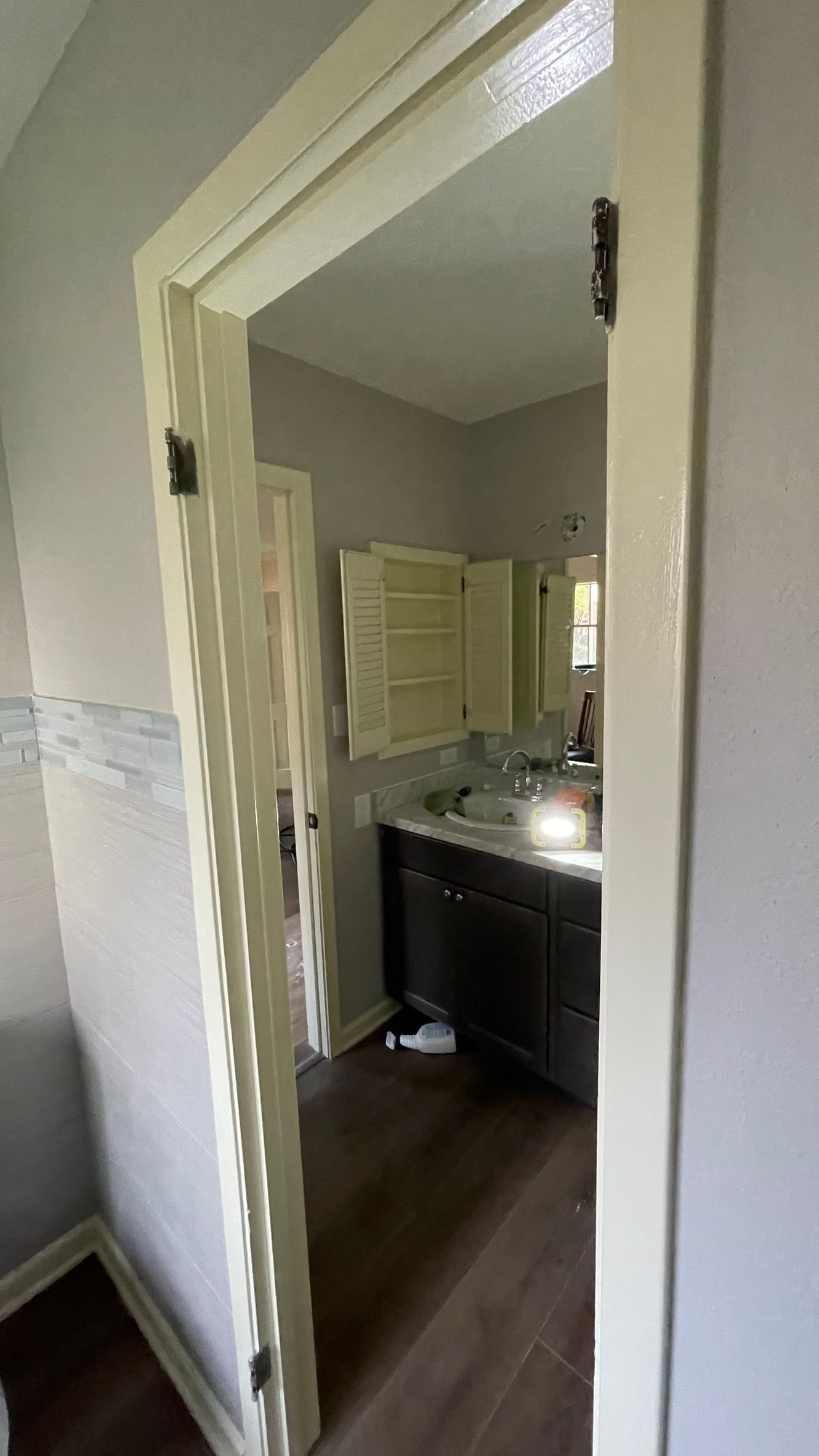 Open doorway leads into a bathroom with dark vanity, light cabinets, and wooden floors.