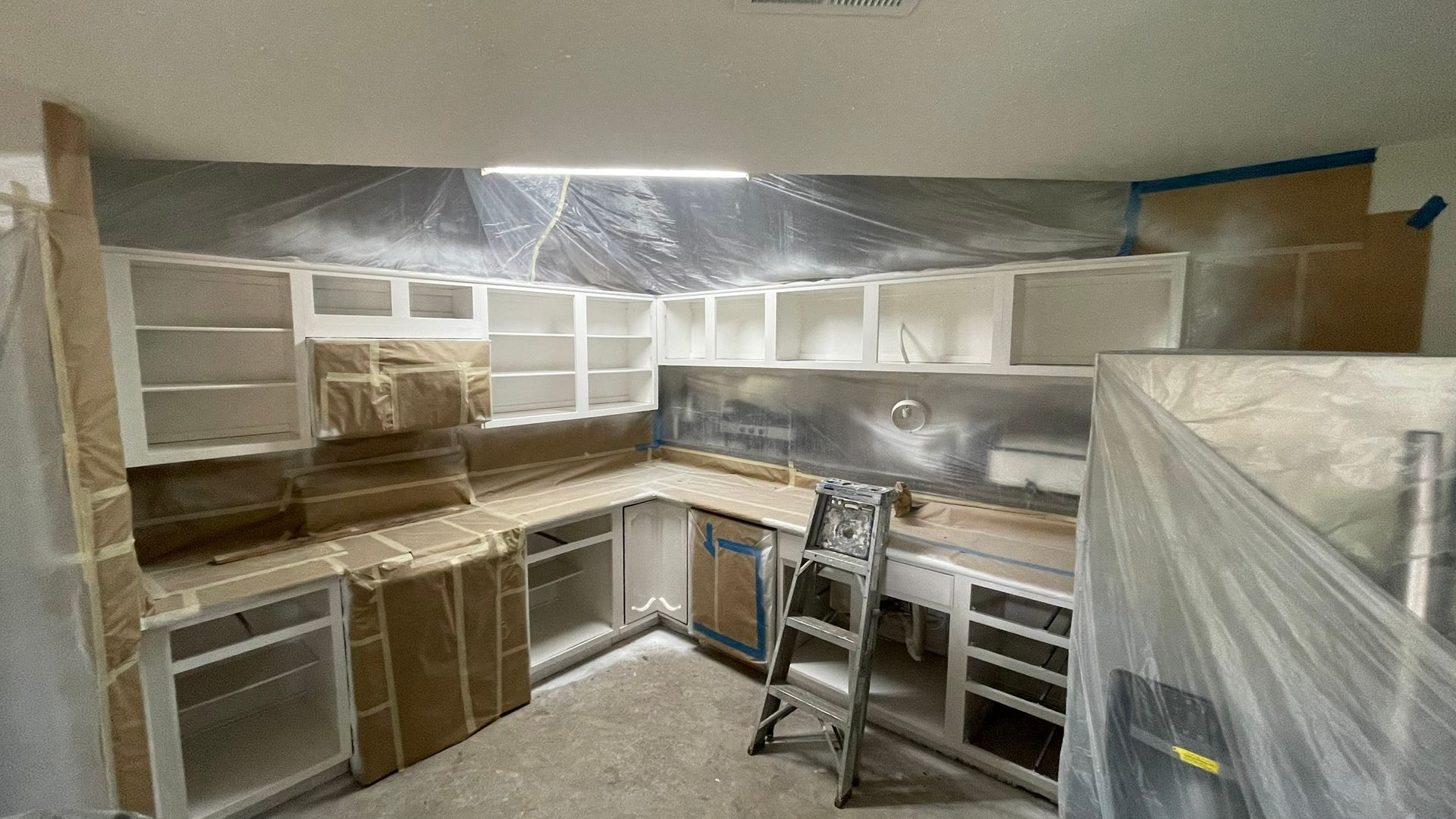 Kitchen being renovated; cabinets, walls, and countertops are covered in protective sheeting and tape.