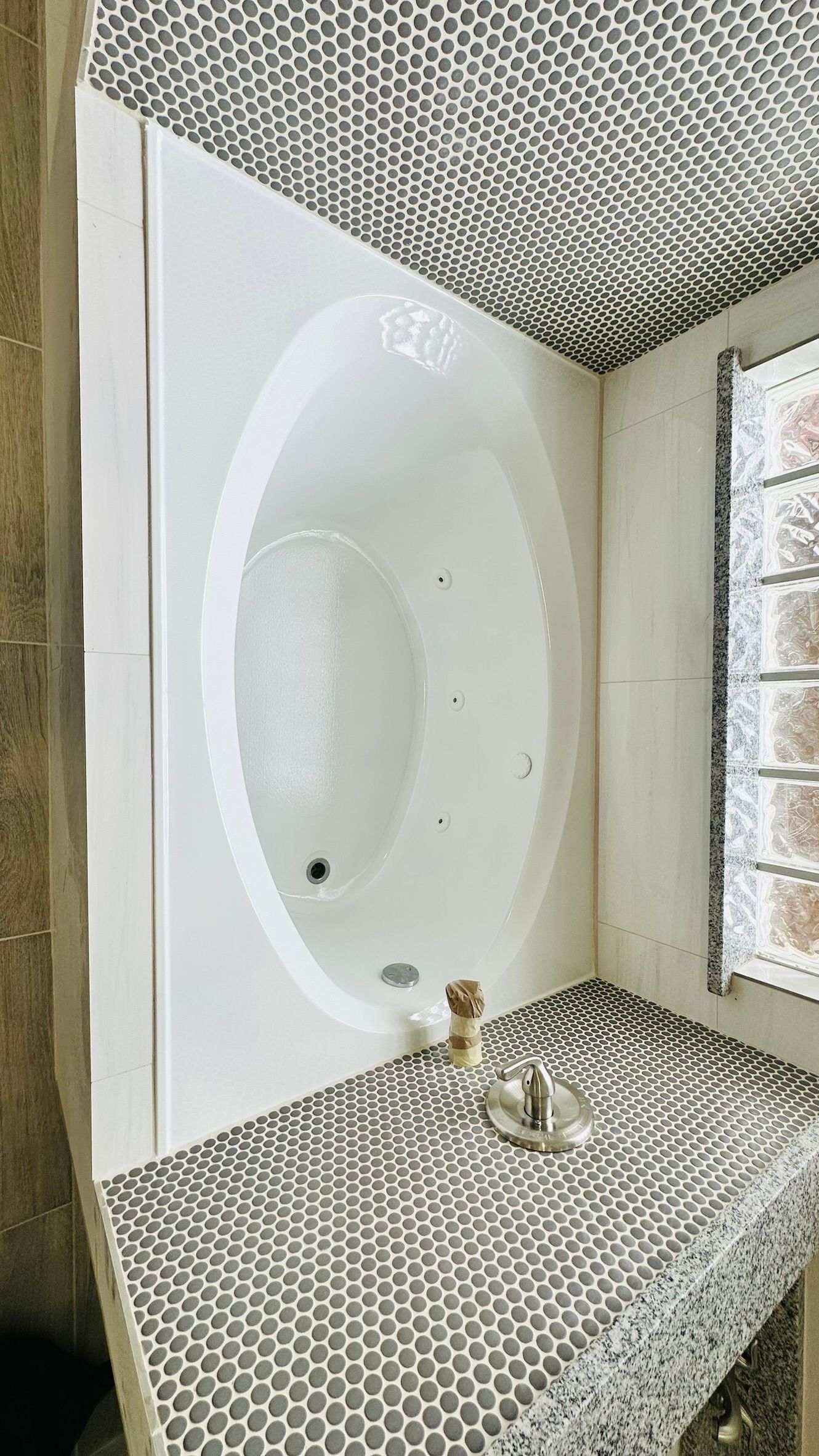 White oval bathtub in a corner bathroom with tiled floor and ceiling.