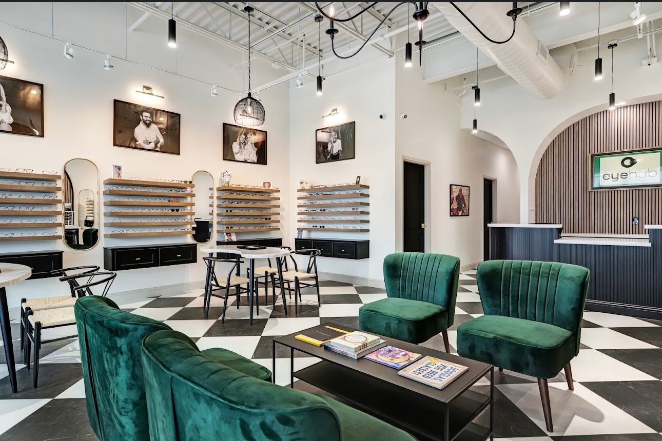 Interior of an eyeglasses store. Green velvet seating and a checkered floor. Frames displayed on walls.