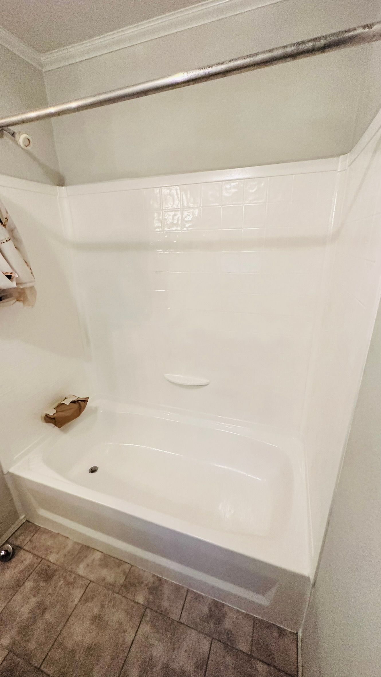 White bathtub and shower surround with a shower rod, set in a bathroom with tile floor.